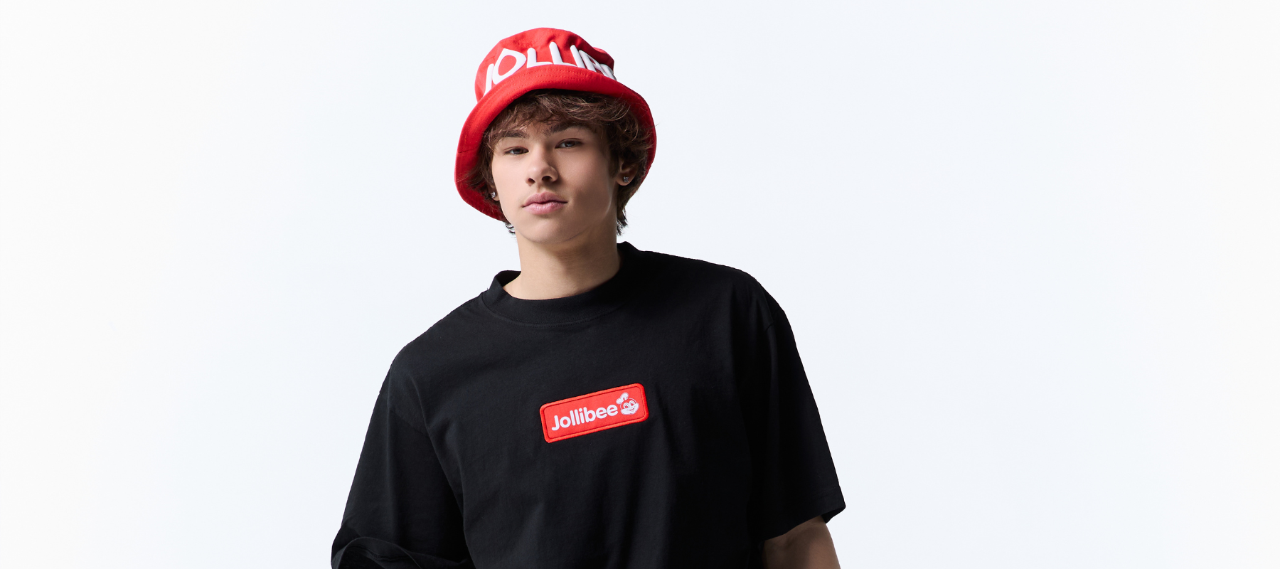 A young man wearing a red Jollibee bucket hat and a black Jollibee t-shirt, standing against a plain white background.