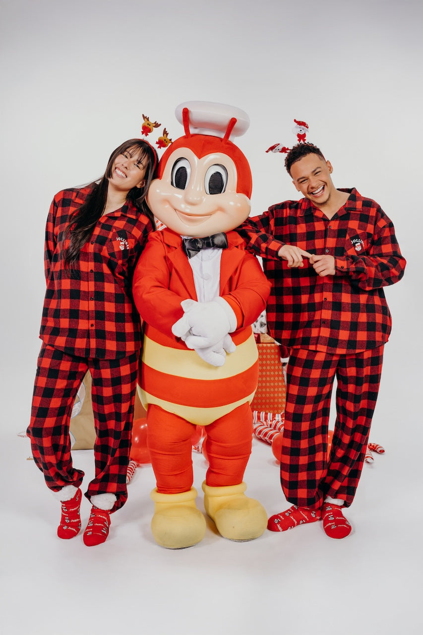 Two people in red and black checkered outfits with the Jollibee mascot on a white background