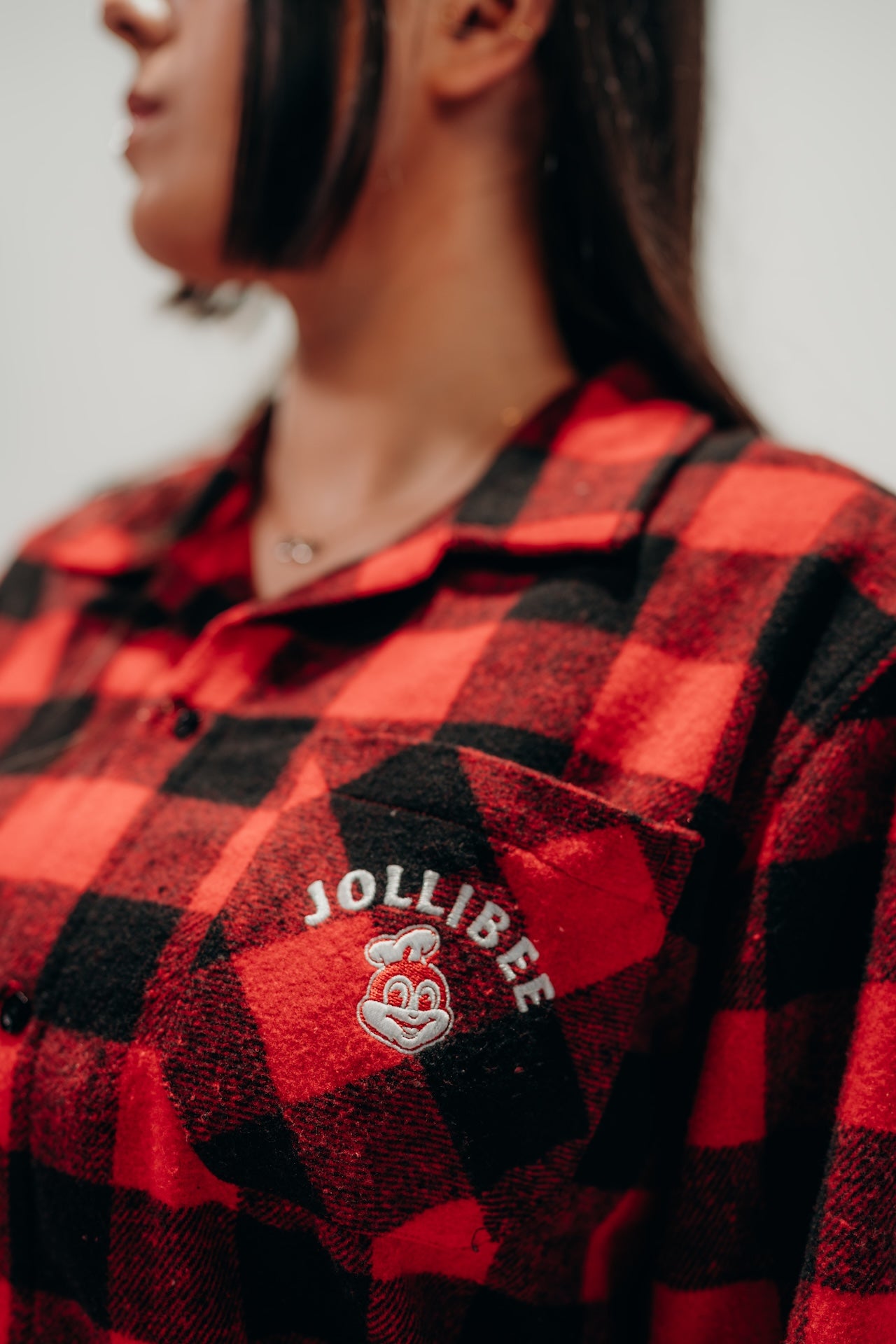 Red and black checkered shirt with Jollibee logo worn by a person
