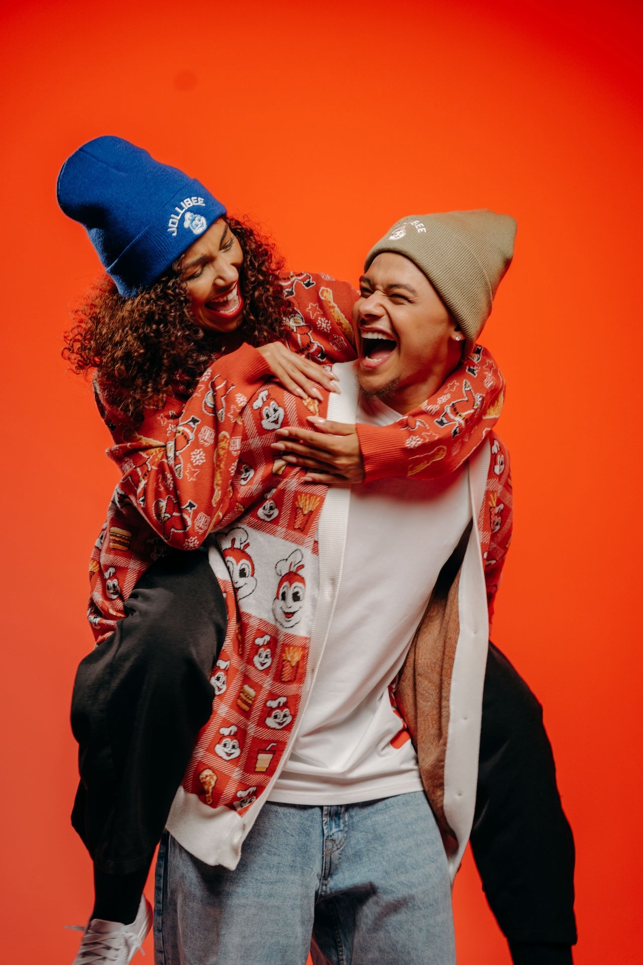 Two people hugging with a colorful Jollibee patterned cardigan on an orange background