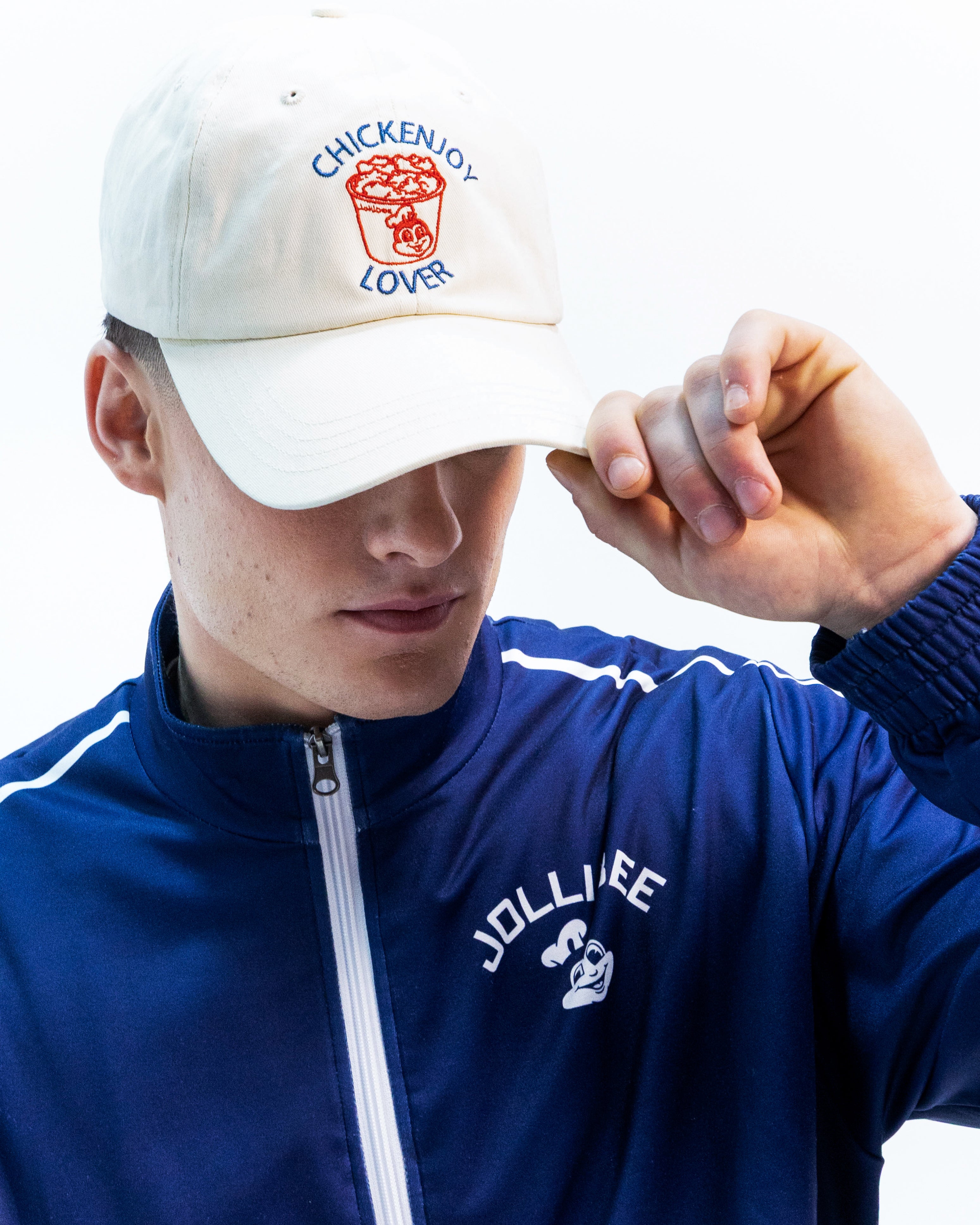 A guy wearing a Jollibee branded tracksuit and white cap with 'CHICKENJOY LOVER' on it.