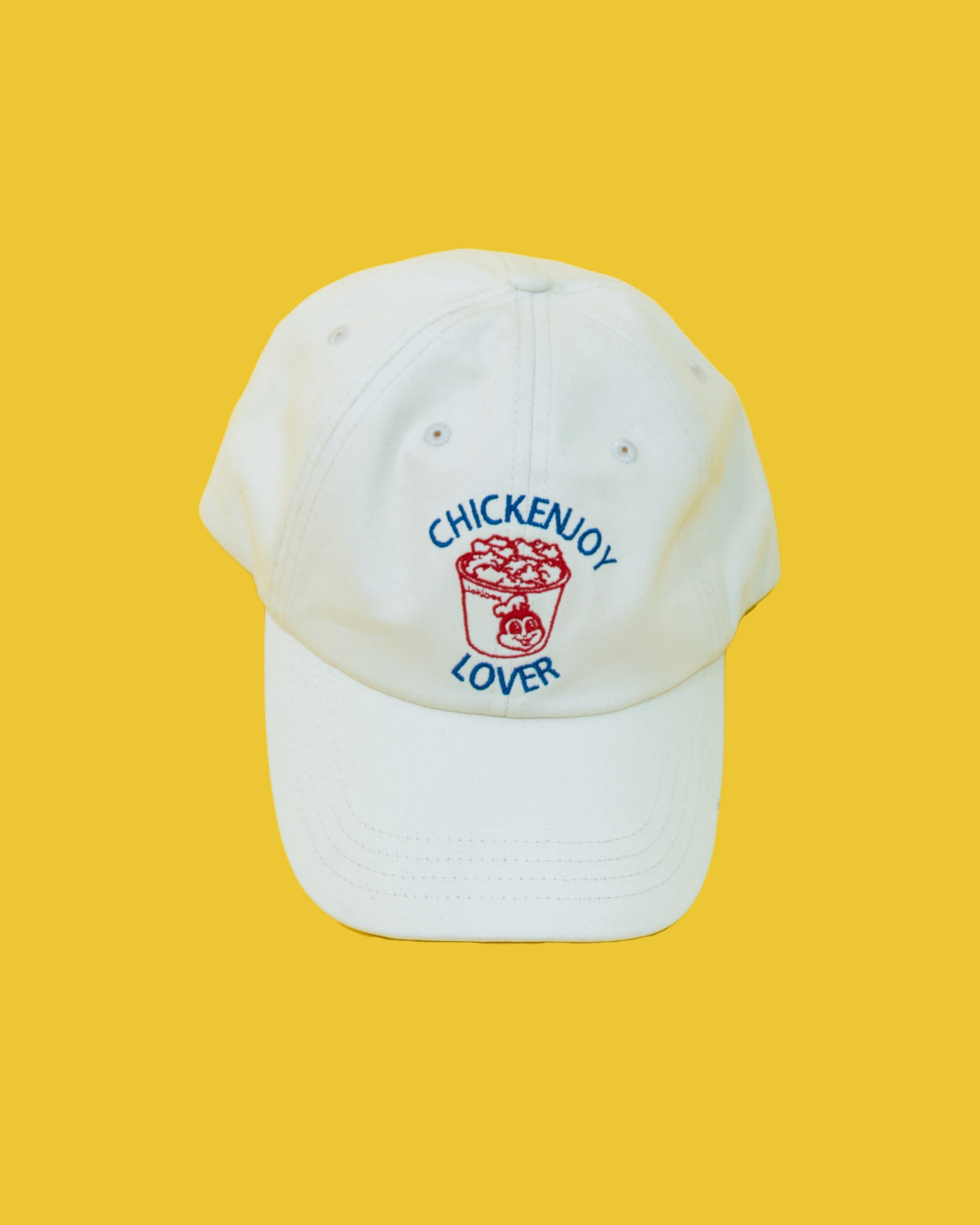 A white baseball cap with 'CHICKENJOY LOVER' text and a graphic emblem on the front against a yellow background.