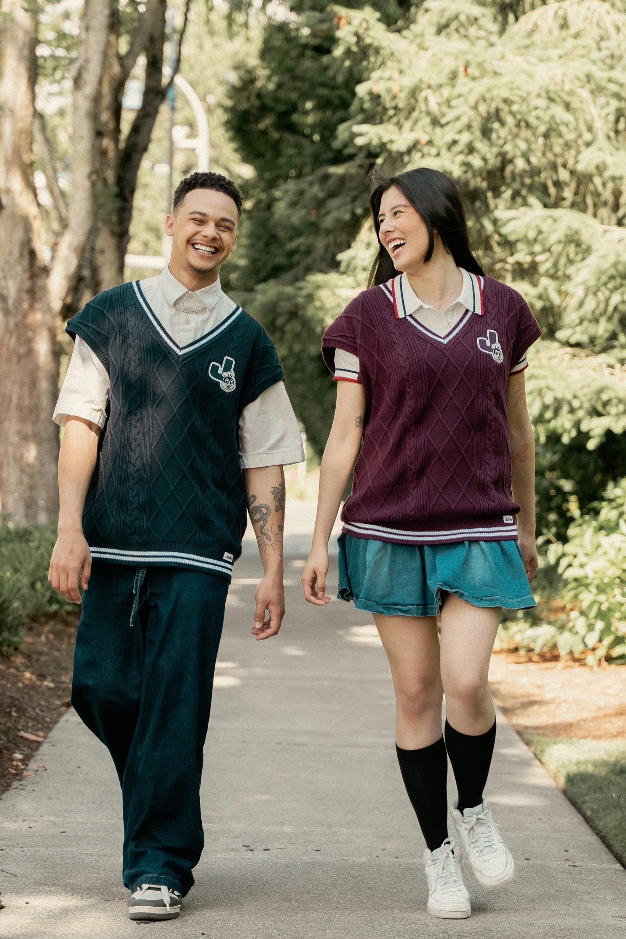 Two people in matching sweater vests walking outdoors on a path with trees in the background.