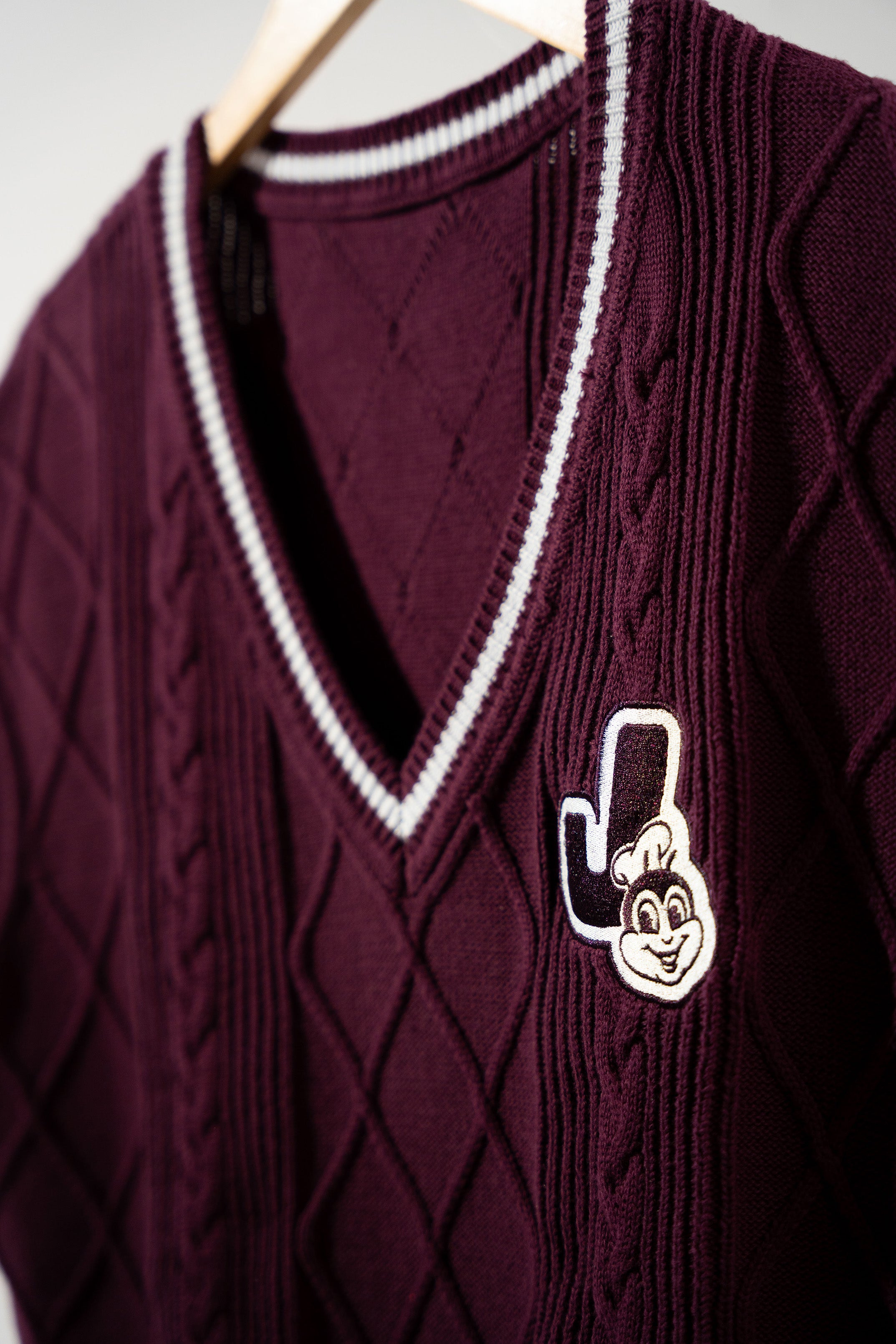 Maroon sweater vest with a Jollibee logo on a white background