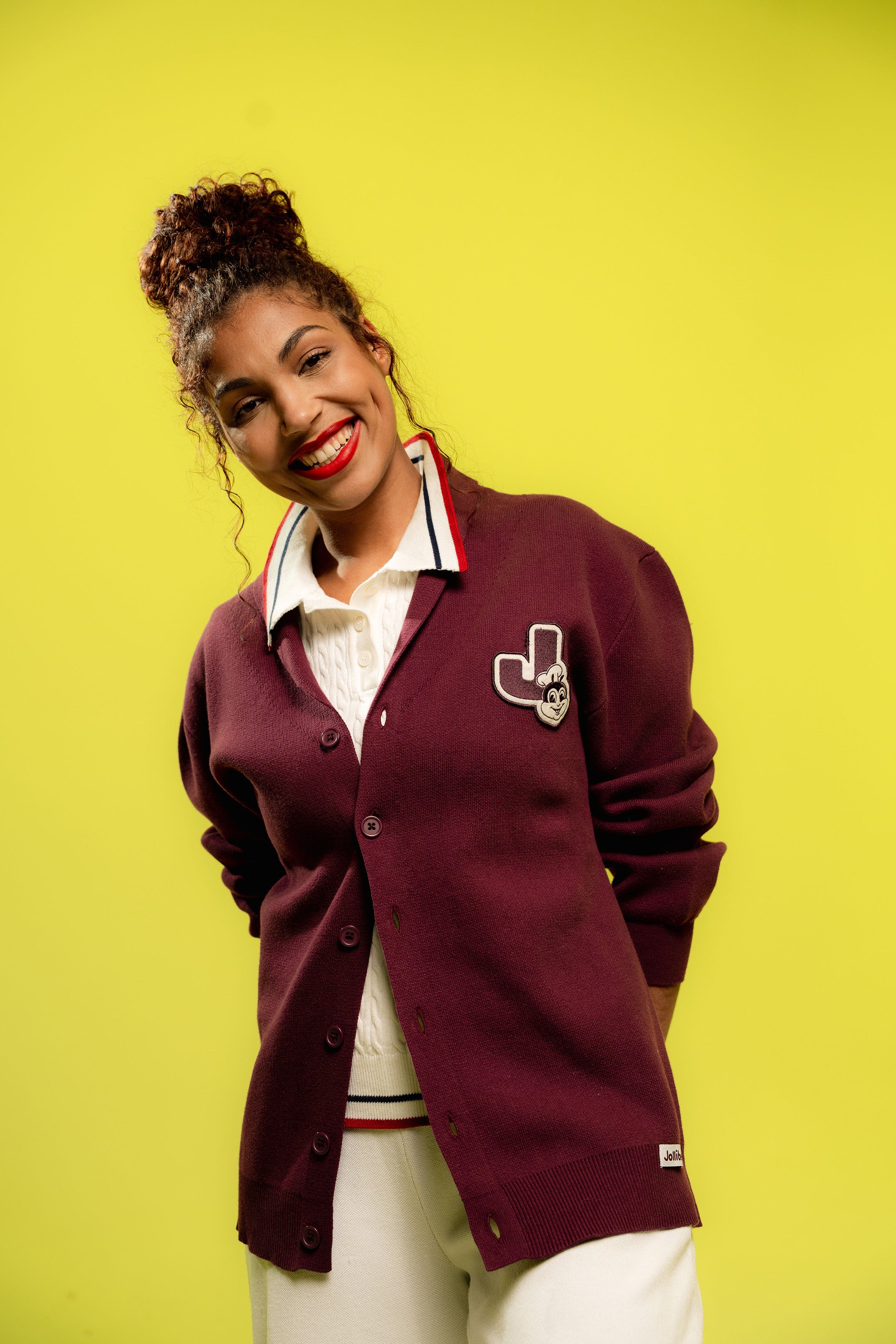 Woman wearing a maroon cardigan with a logo on a yellow background