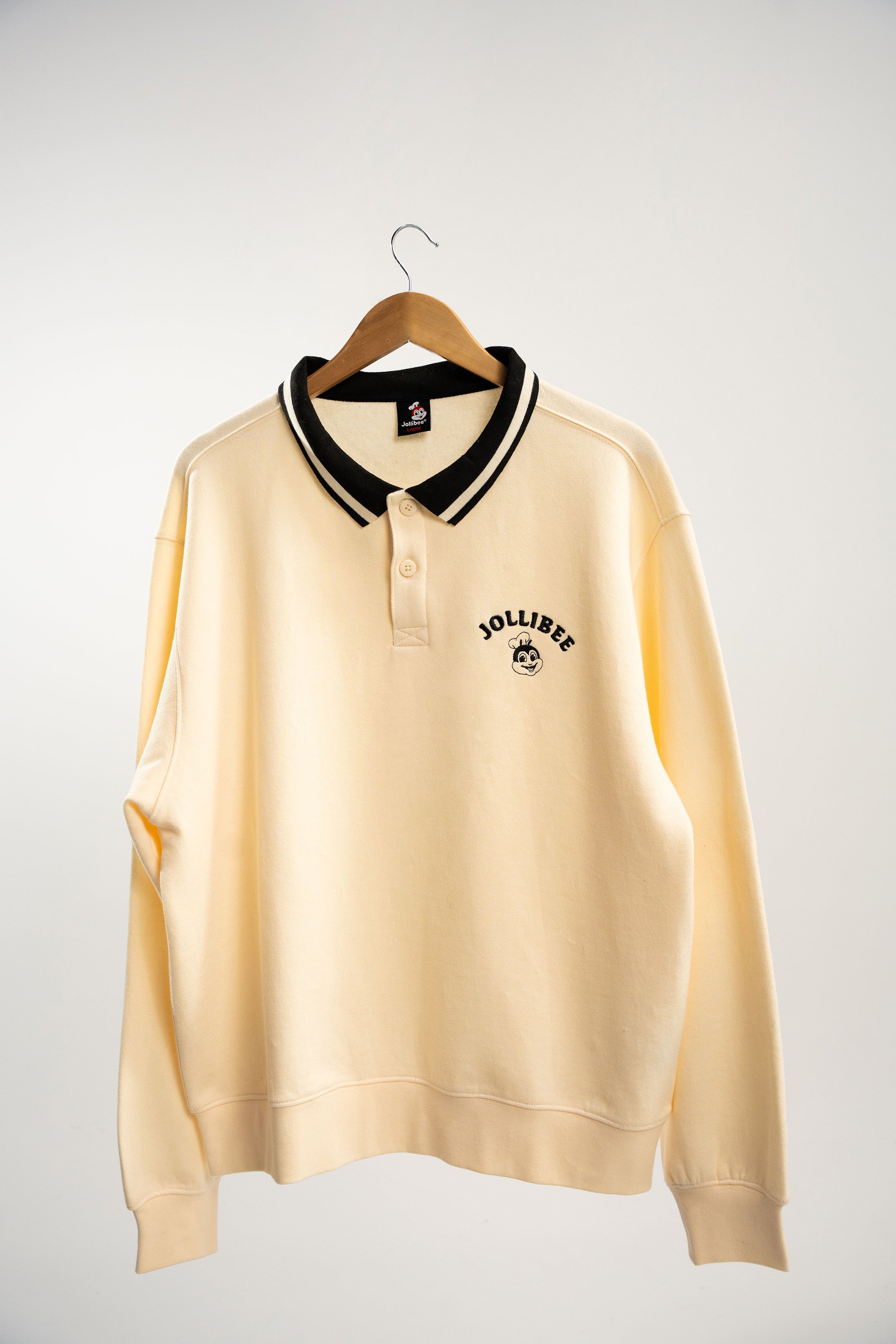 Beige sweater with black collar on a hanger against a white background