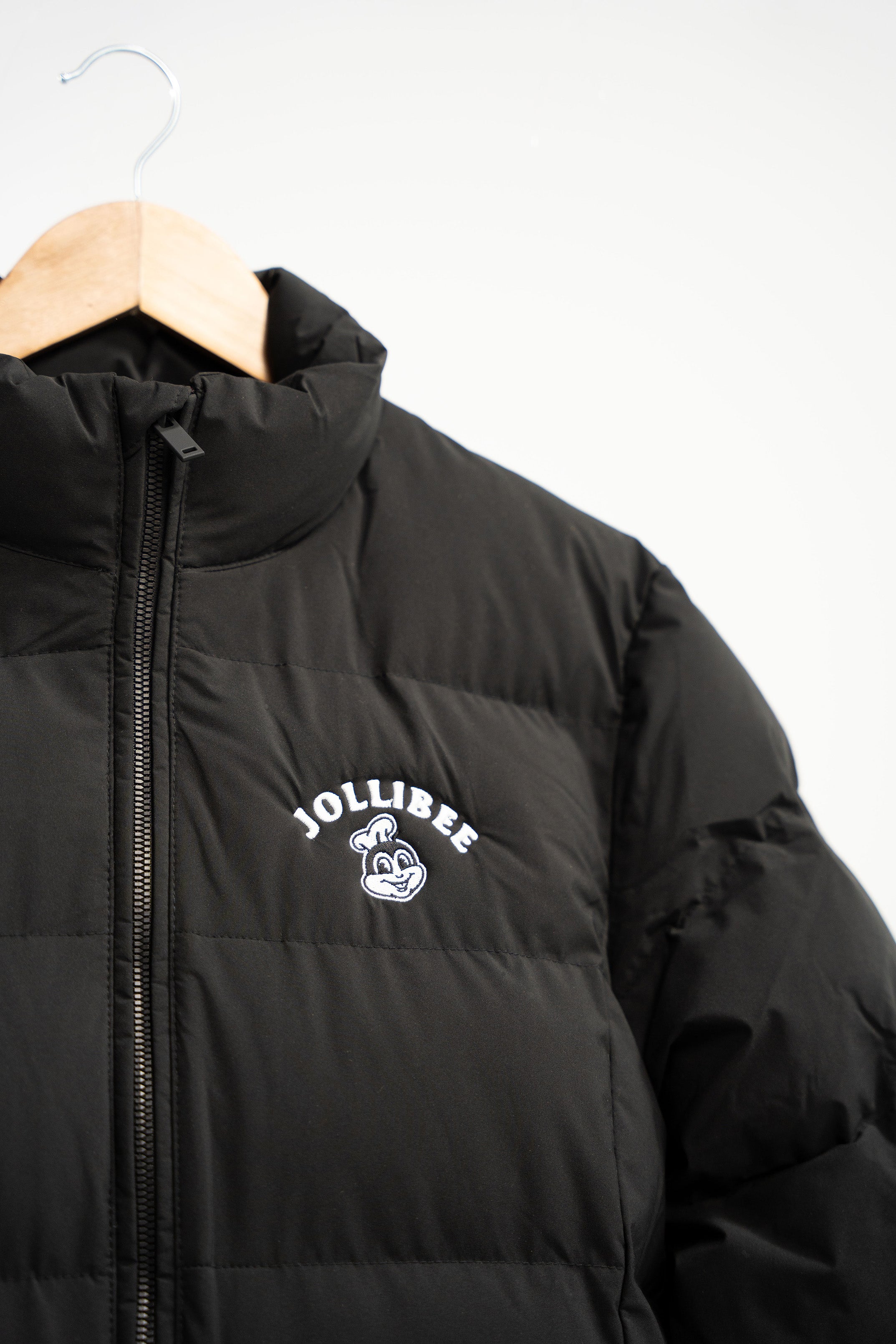 Black puffer jacket with Jollibee logo on a hanger against a white background