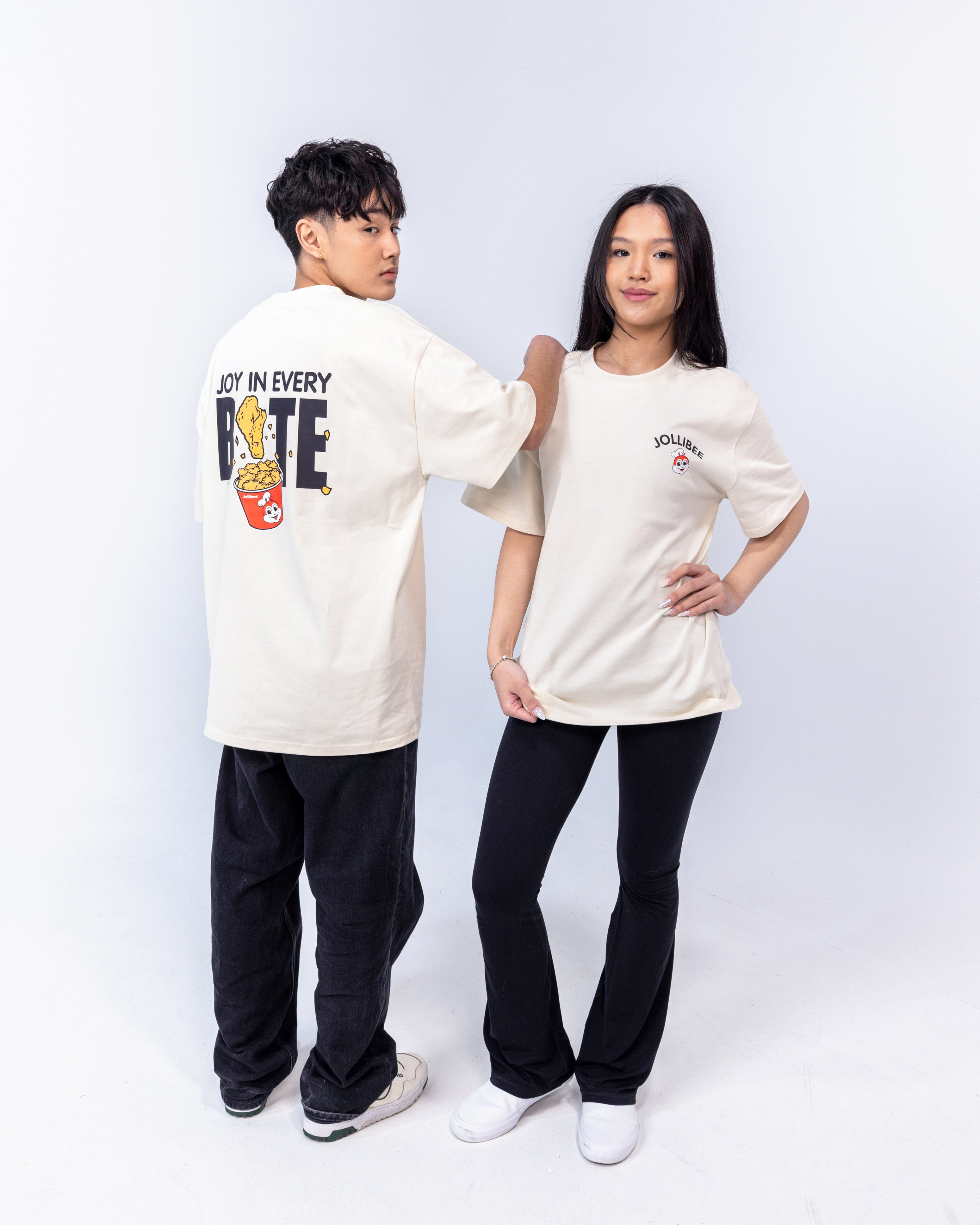 Guy and a girl both wearing cream-colored tees with the Jollibee logo printed in front, and 'JOY IN EVERYBITE' on the back.