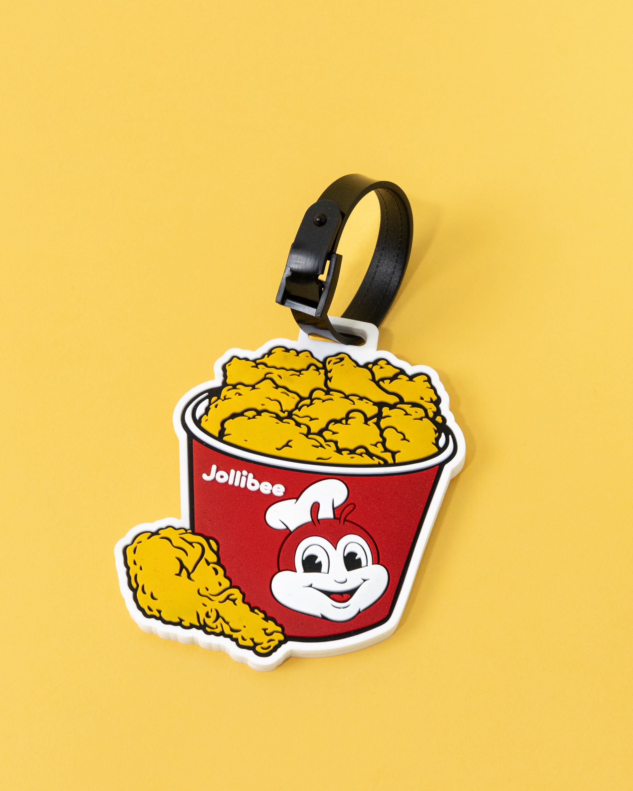 A red and white luggage tag with a Jollibee fried chicken bucket design, attached to a black strap.