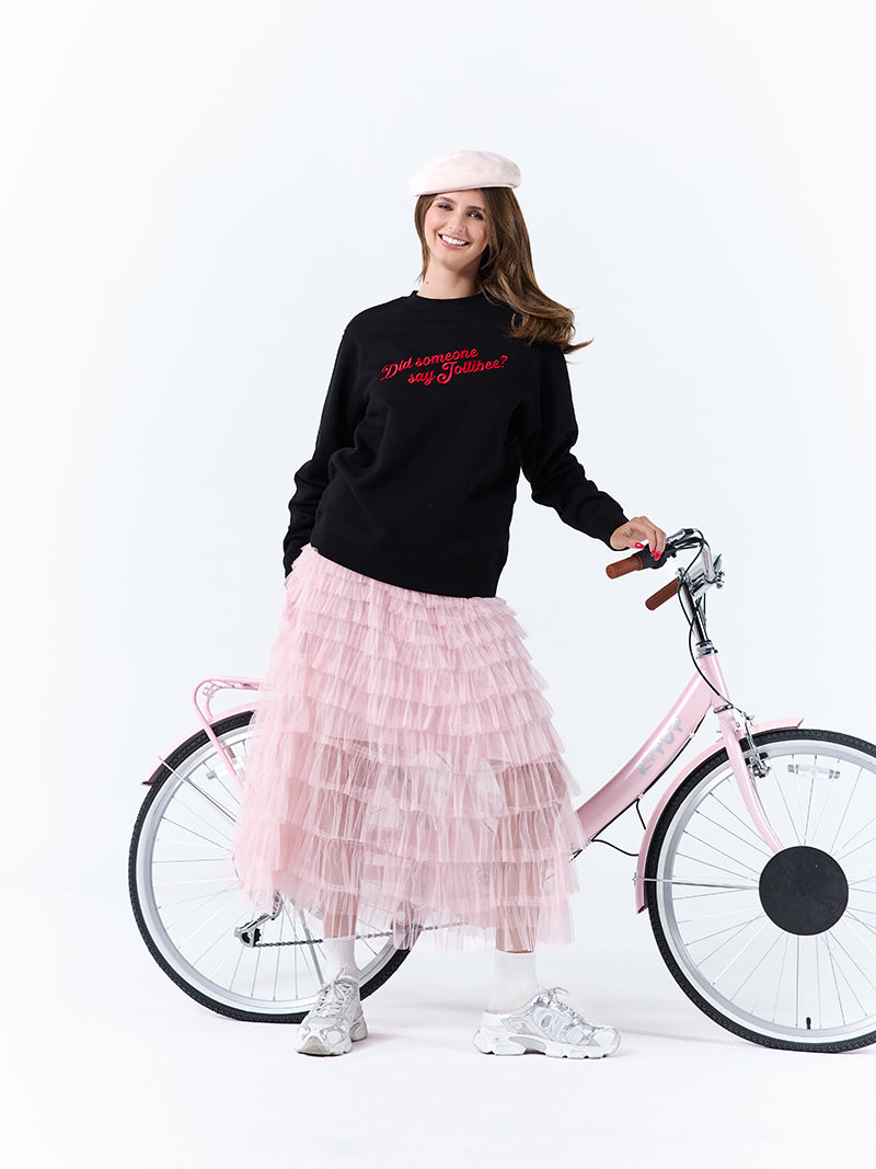 A young woman wearing a black crewneck sweatshirt with a 'Did someone say Jollibee?' text across the chest holding on to a pink bike on a white background.