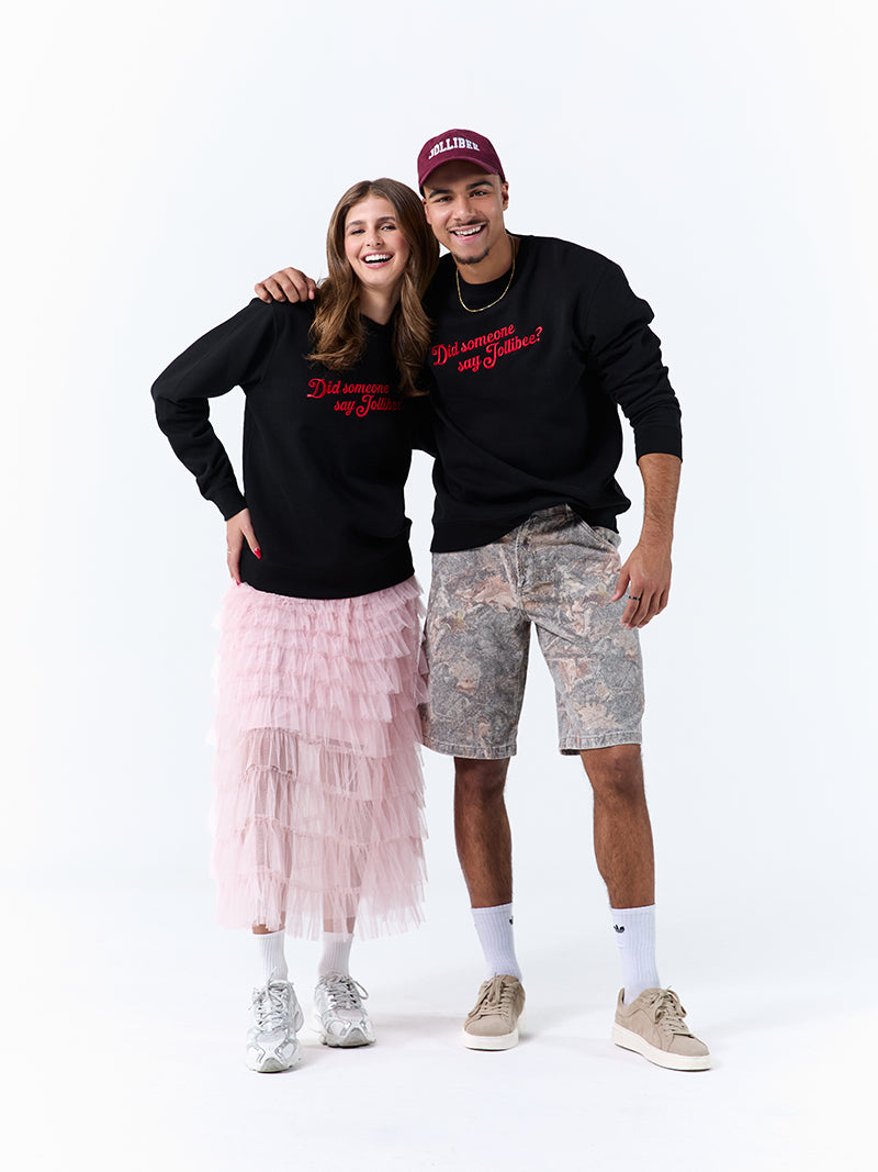 A young woman and young man wearing a black crewneck sweatshirt with a 'Did someone say Jollibee?' text across the chest on a white background.
