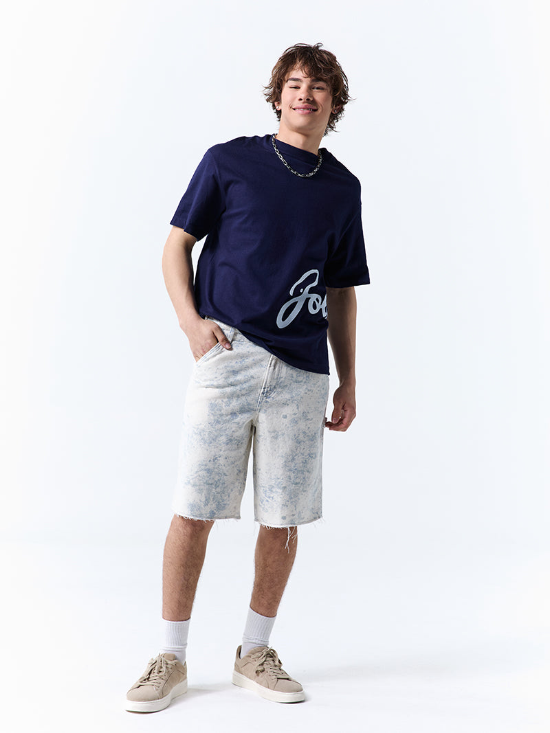 A young man wearing a navy t-shirt with 'Jollibee' in script on the side on a white background.