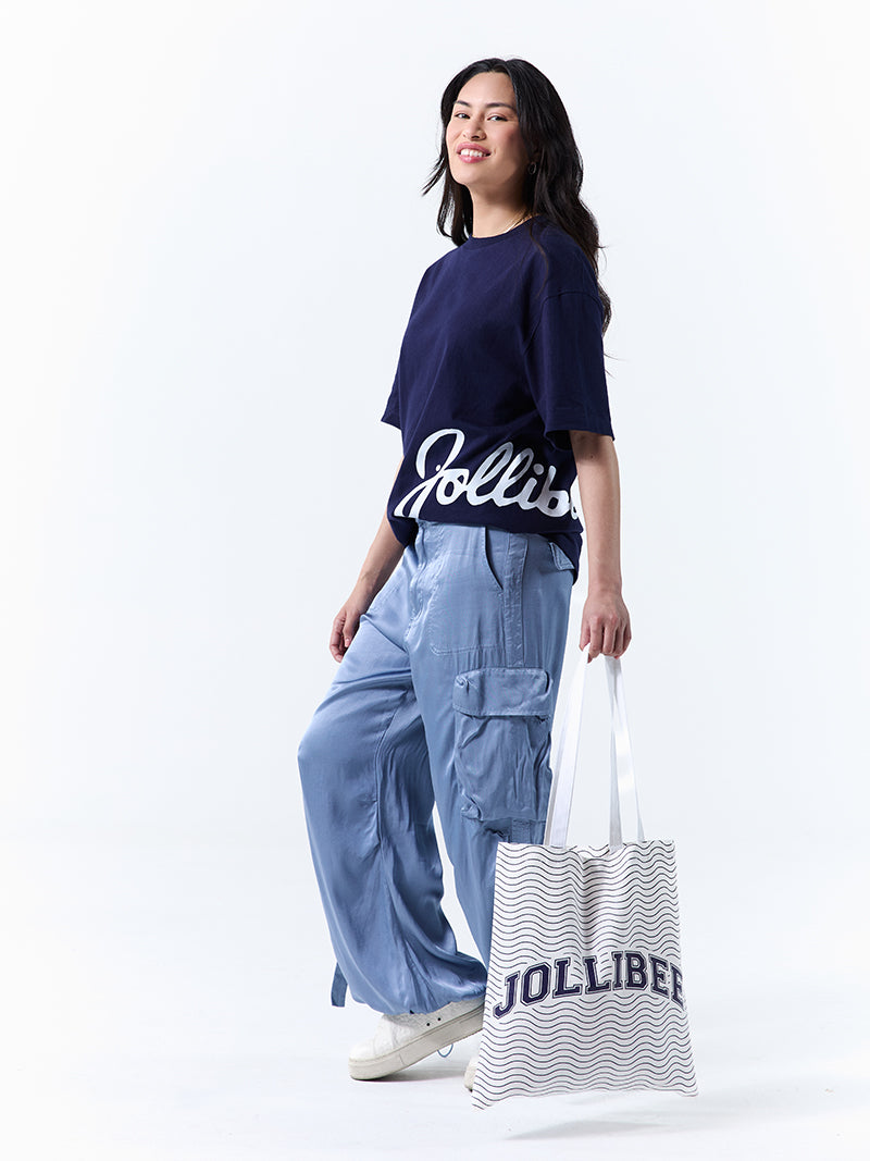 A young woman wearing a navy t-shirt with 'Jollibee' in script on the side, holding a tote bag, on a white background.