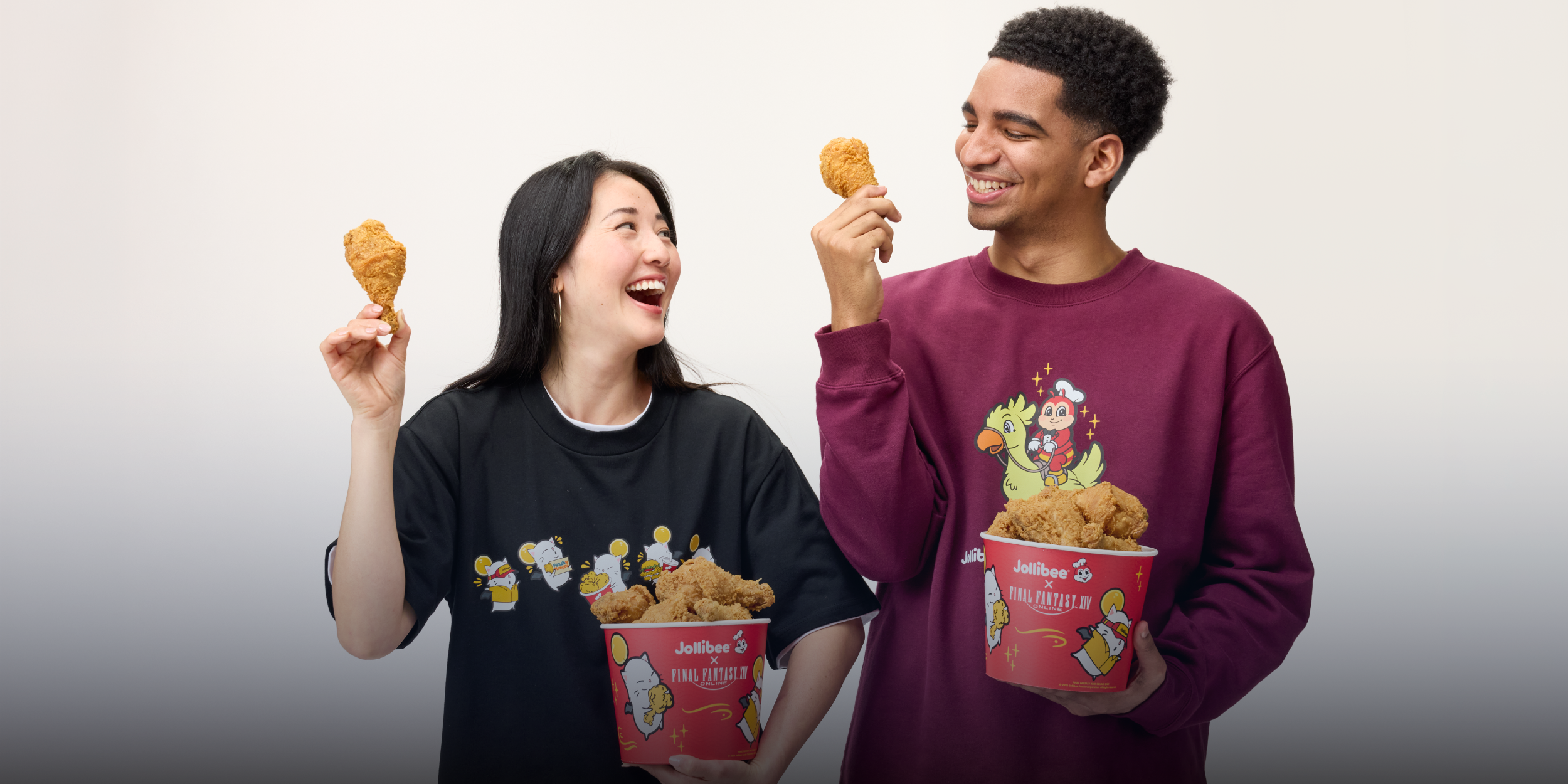 Two people holding fried chicken and wearing Jollibee and FINAL FANTASY XIV themed sweatshirts against a plain background
