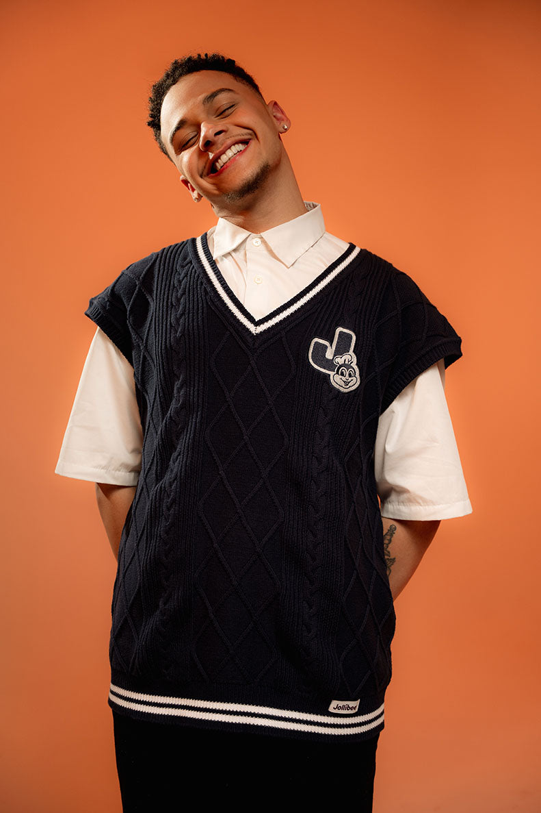 Man wearing a black varsity vest over a white shirt with an orange background
