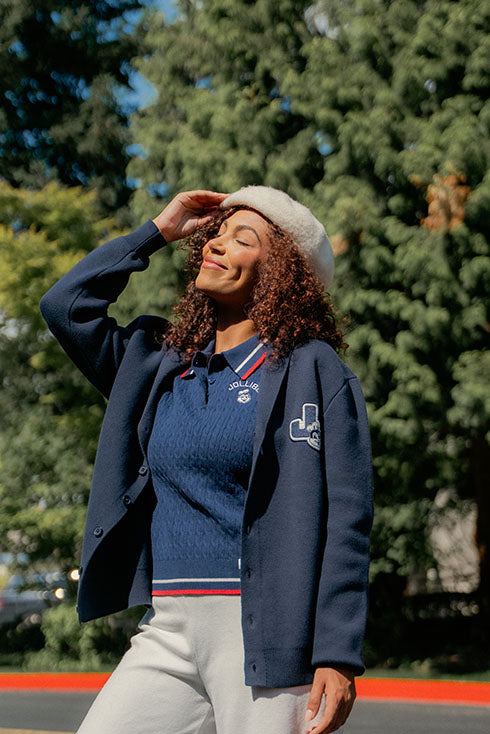 Woman wearing a navy blue cardigan over a blue shirt with a Jollibee logo, standing outdoors with trees in the background.