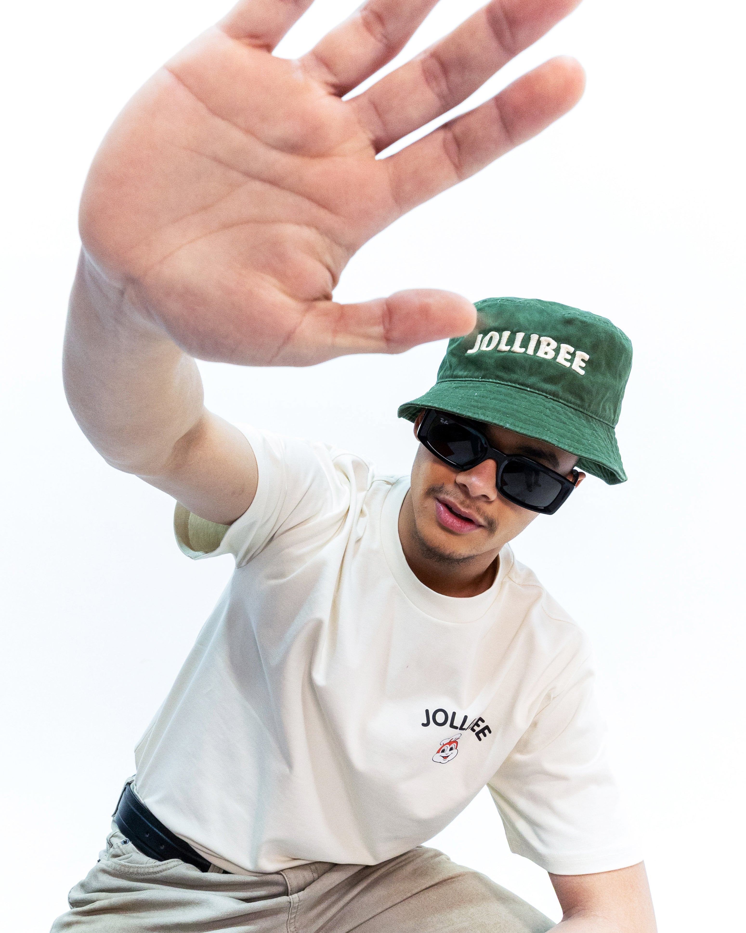 Person wearing a green cap with 'Jollibee' branding, white t-shirt, and sunglasses on a white background