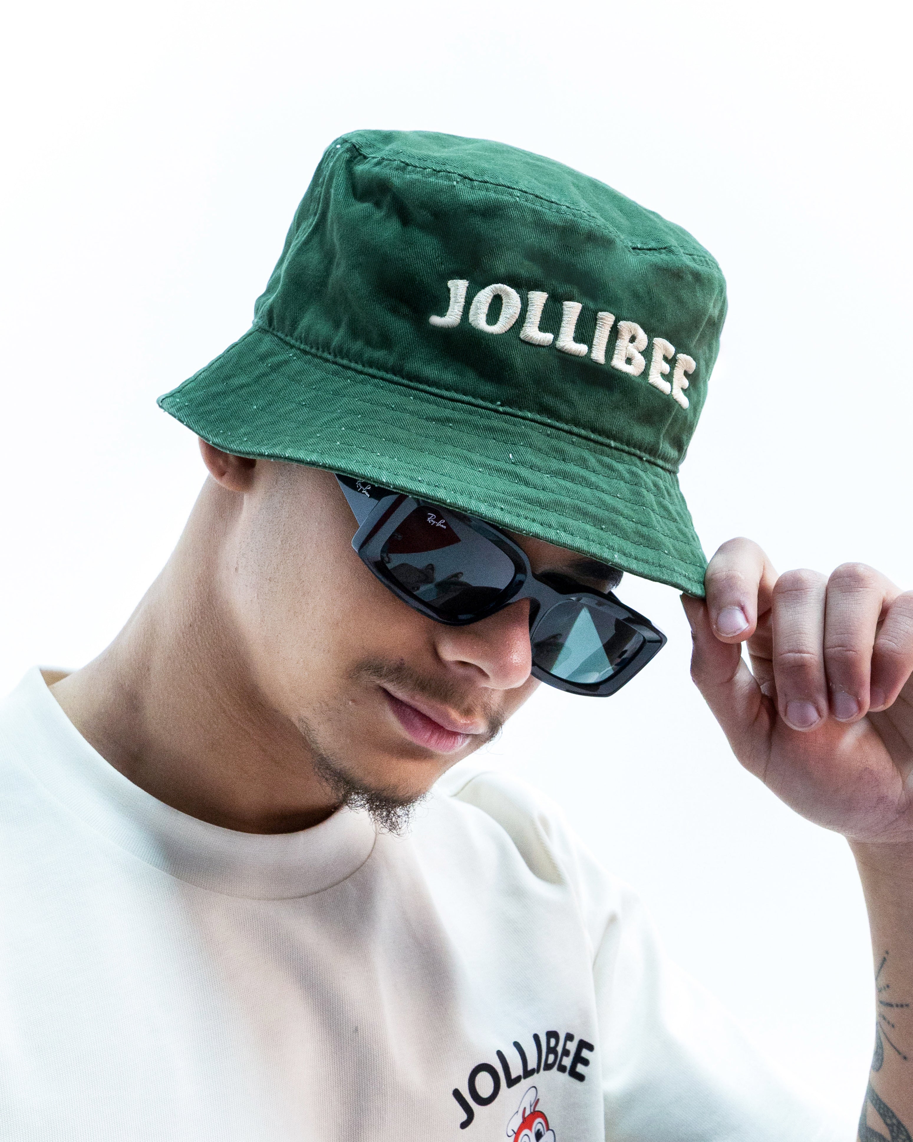 Person wearing a green 'Jollibee' hat and sunglasses with a white shirt featuring the brand logo.