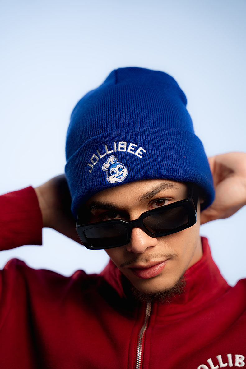 Person wearing a blue beanie with Jollibee logo and red jacket on light gray background