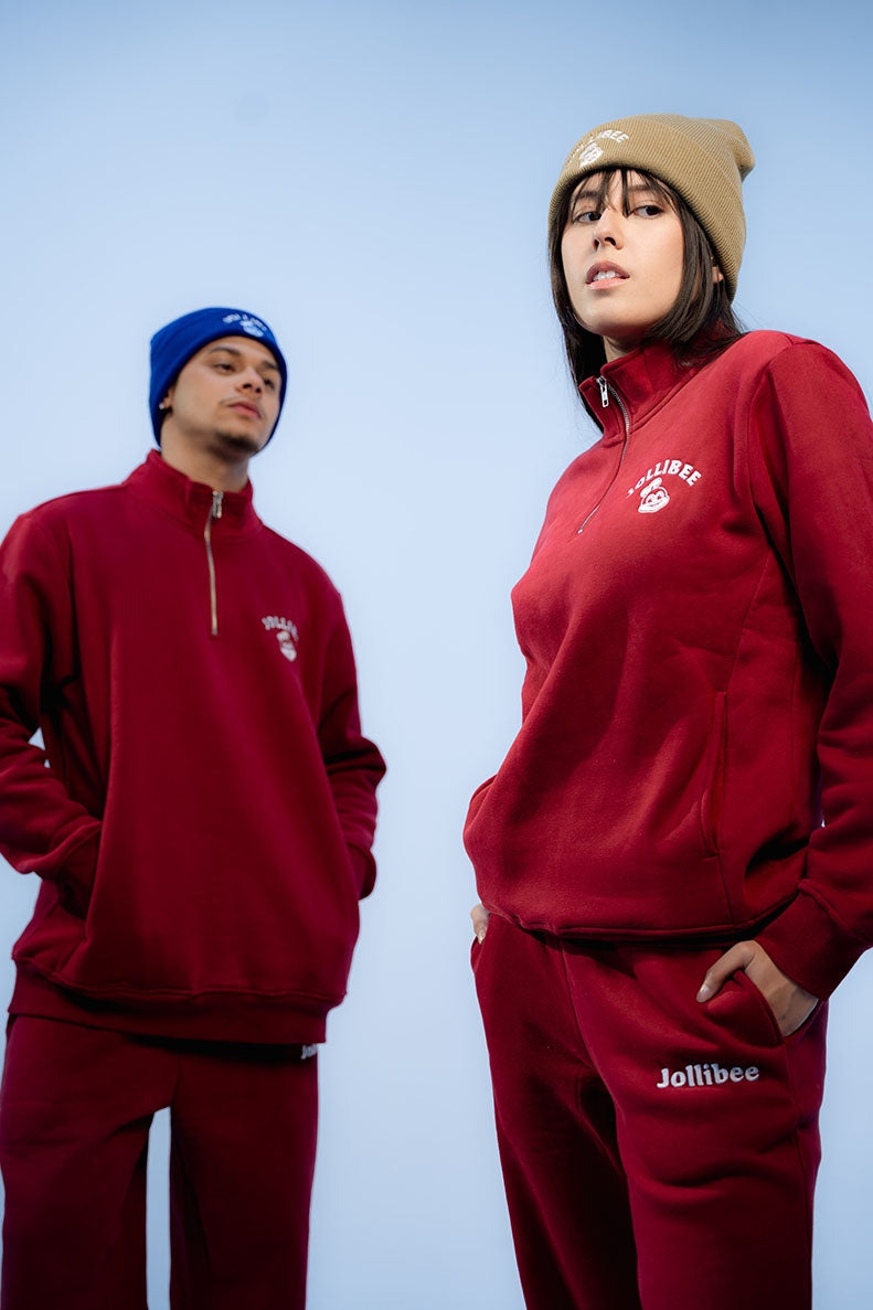 Two people wearing red tracksuits with visible Jollibee logo against a light blue background