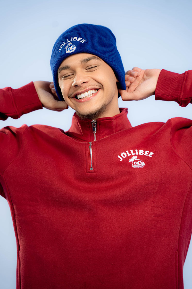 Person wearing a red Jollibee sweatshirt and blue beanie against a light blue background