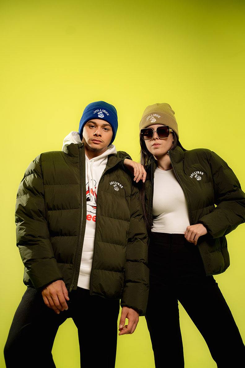 Two people wearing green jackets and beanies against a yellow background