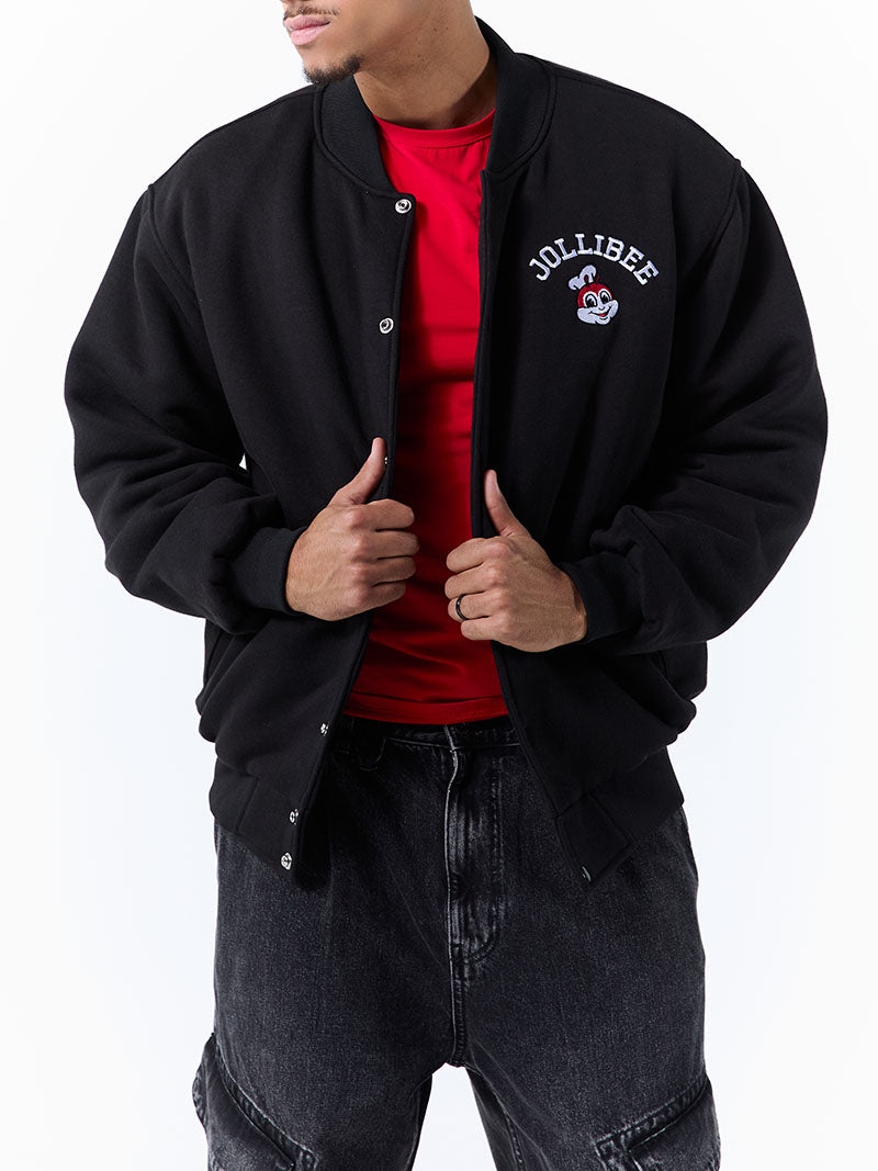 Person wearing a black letterman jacket with a logo, red shirt, and dark jeans on a white background