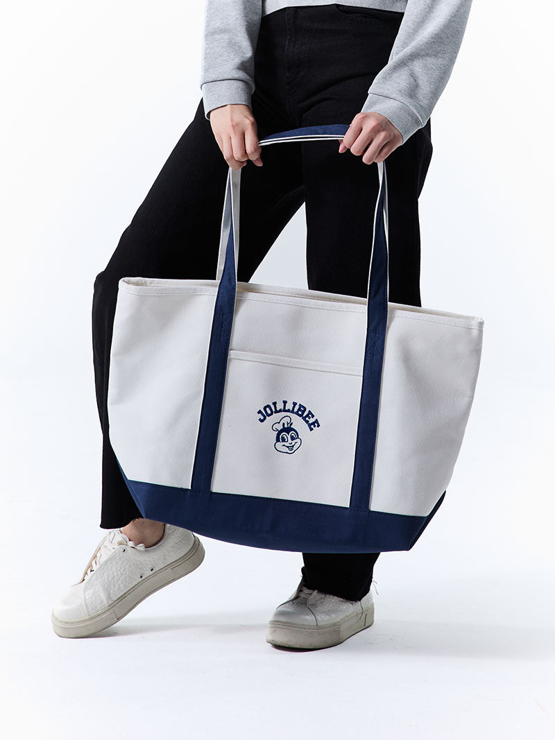 Person holding a white tote bag with navy handles and a Jollibee logo on a white background