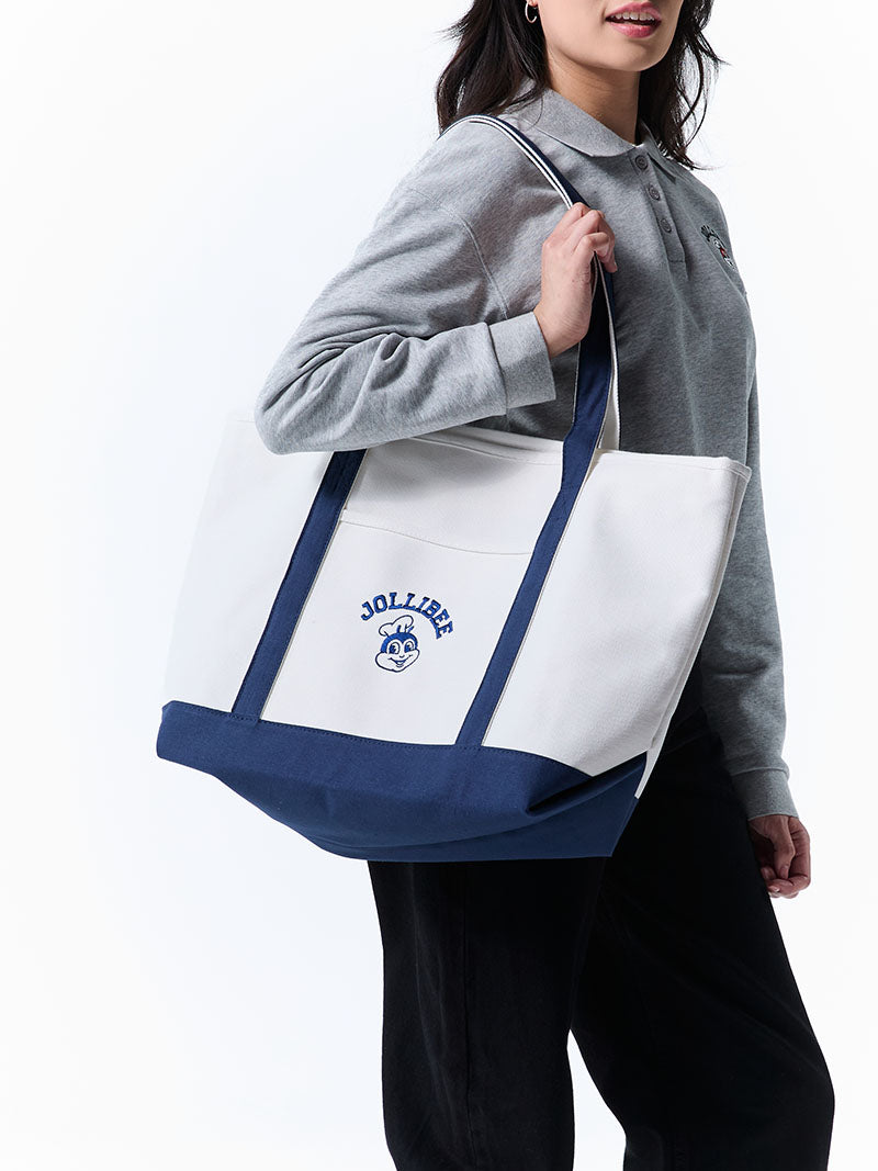 Person holding a white tote bag with blue accents and 'Jollibee' branding.