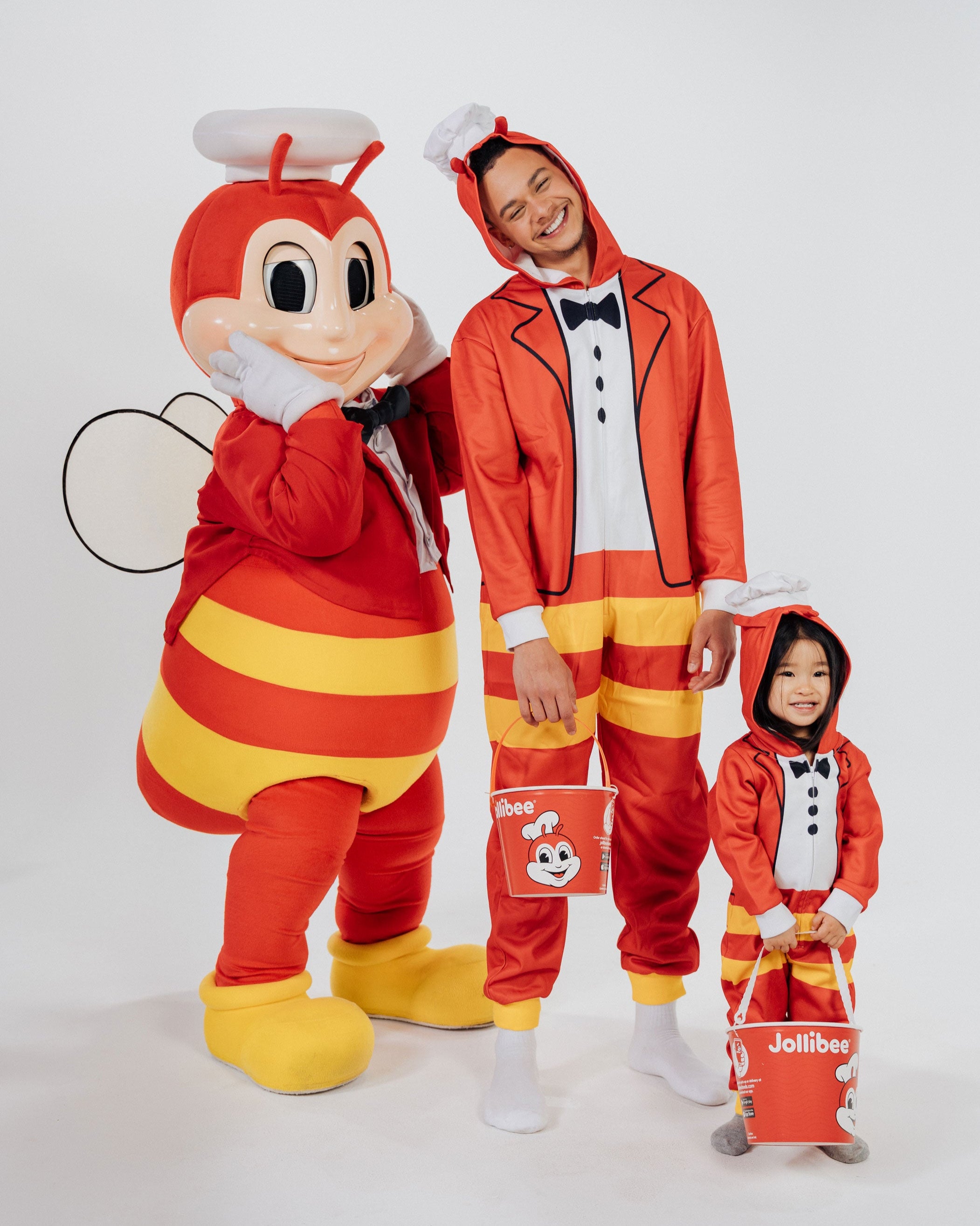Jollibee mascot with a person in a red and yellow Jollibee onesie with a child in matching outfits on a white background