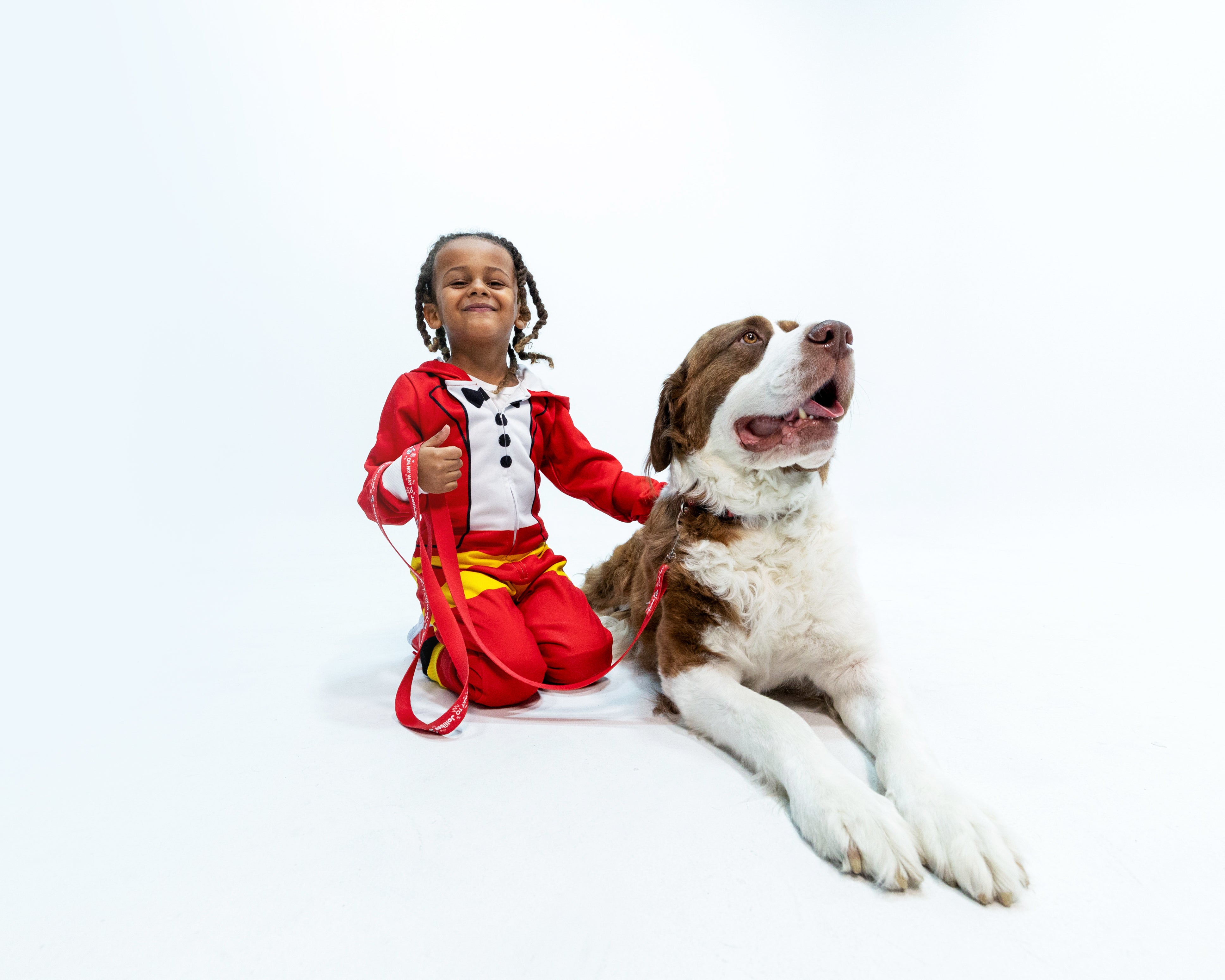 Child in a Jollibee onesie with a large dog on a white background