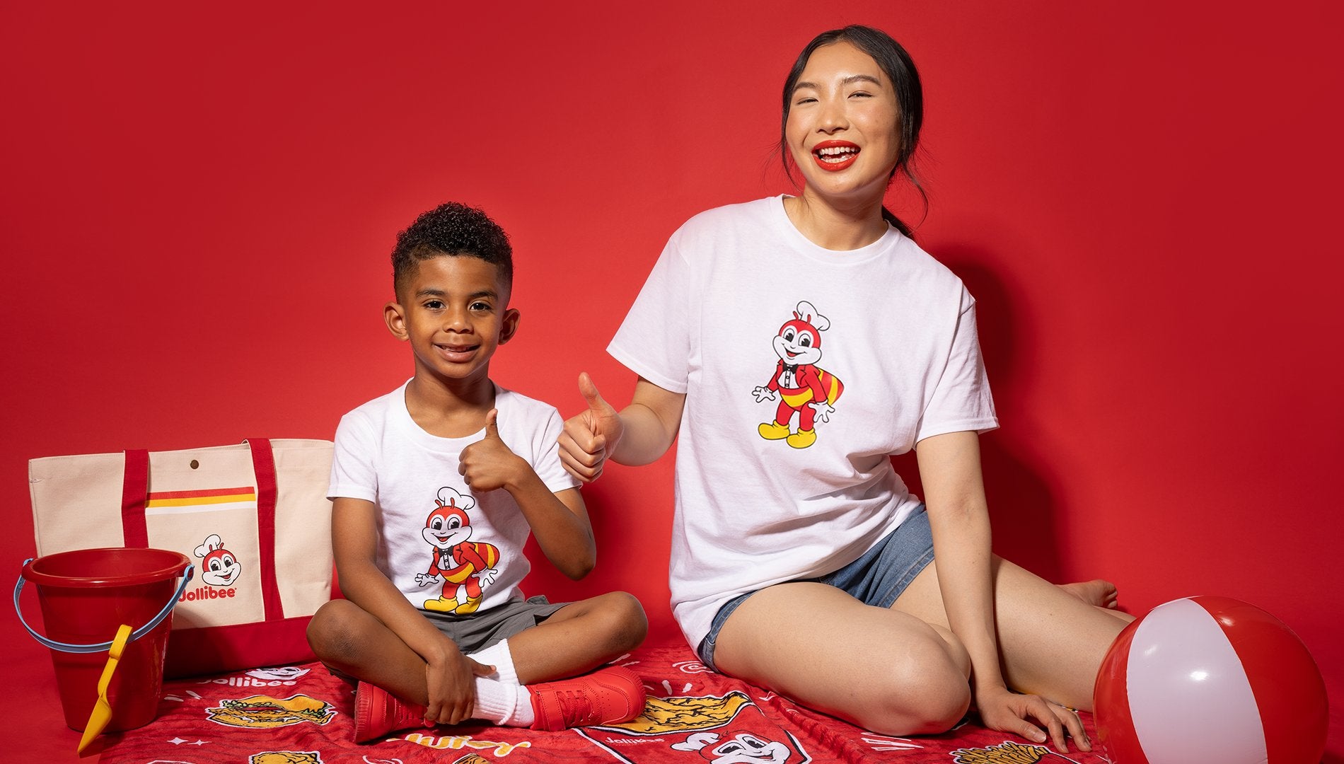 a boy and a young woman happily sitting down with their thumbs up and wearing Jollibee merch