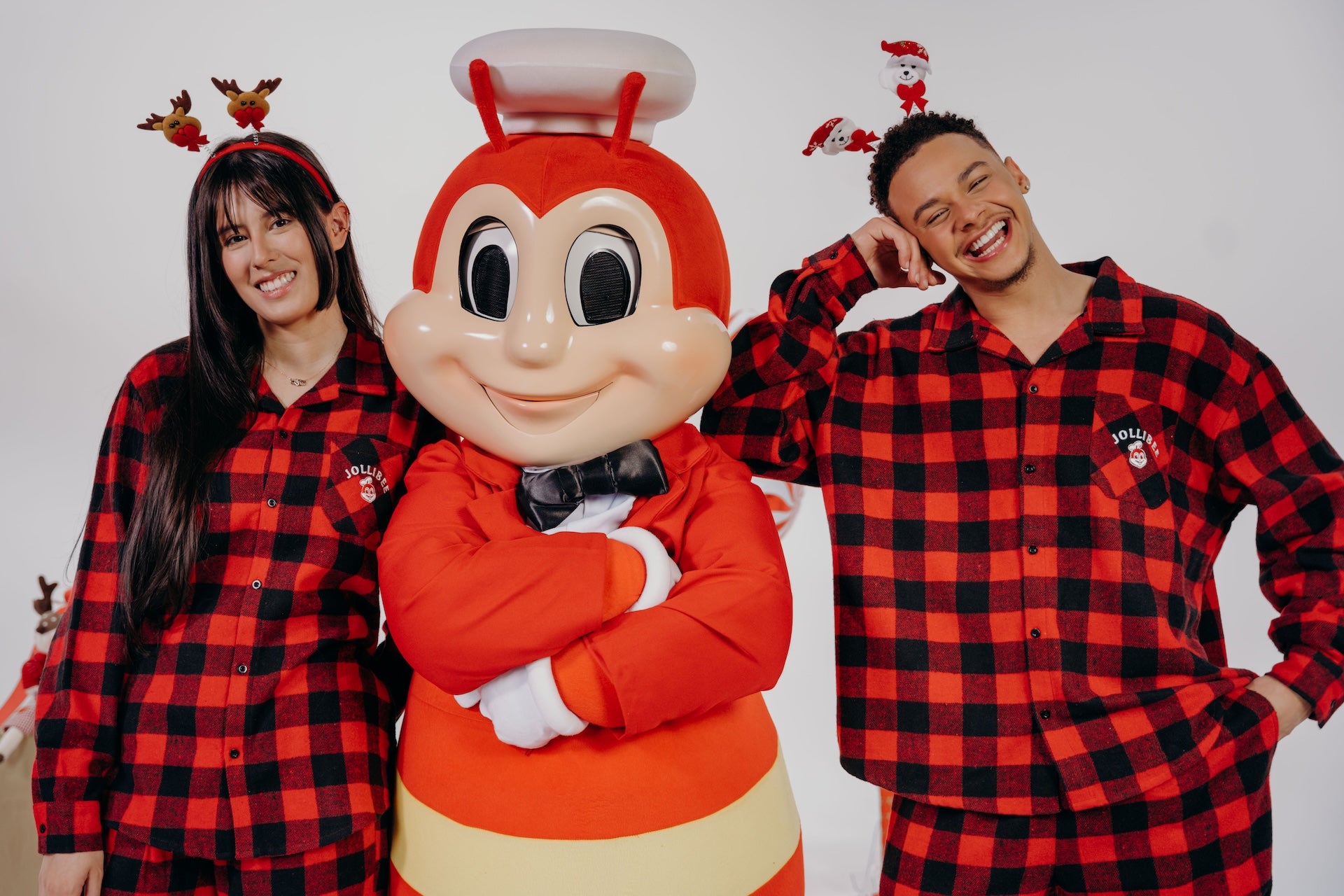 Two people in red and black checkered pajamas with the Jollibee mascot on a white background