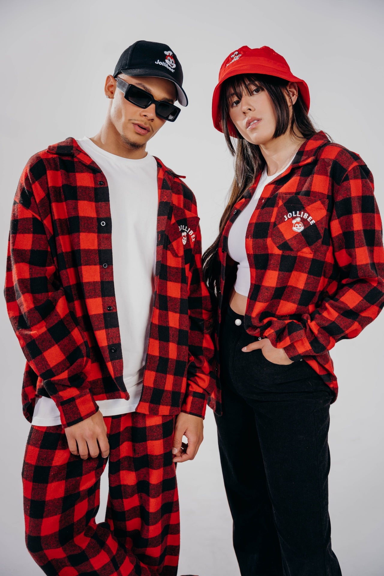 Two people wearing red and black checkered outfits with hats on a plain background