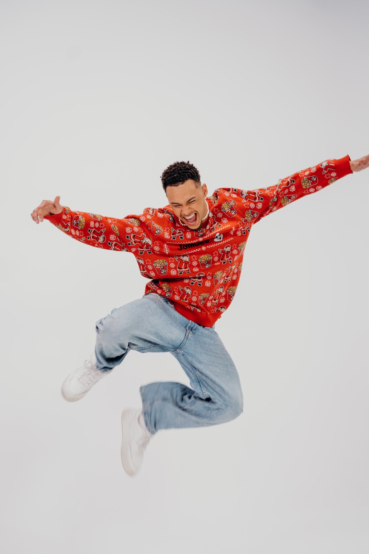Person wearing a red patterned sweater and blue jeans jumping against a white background