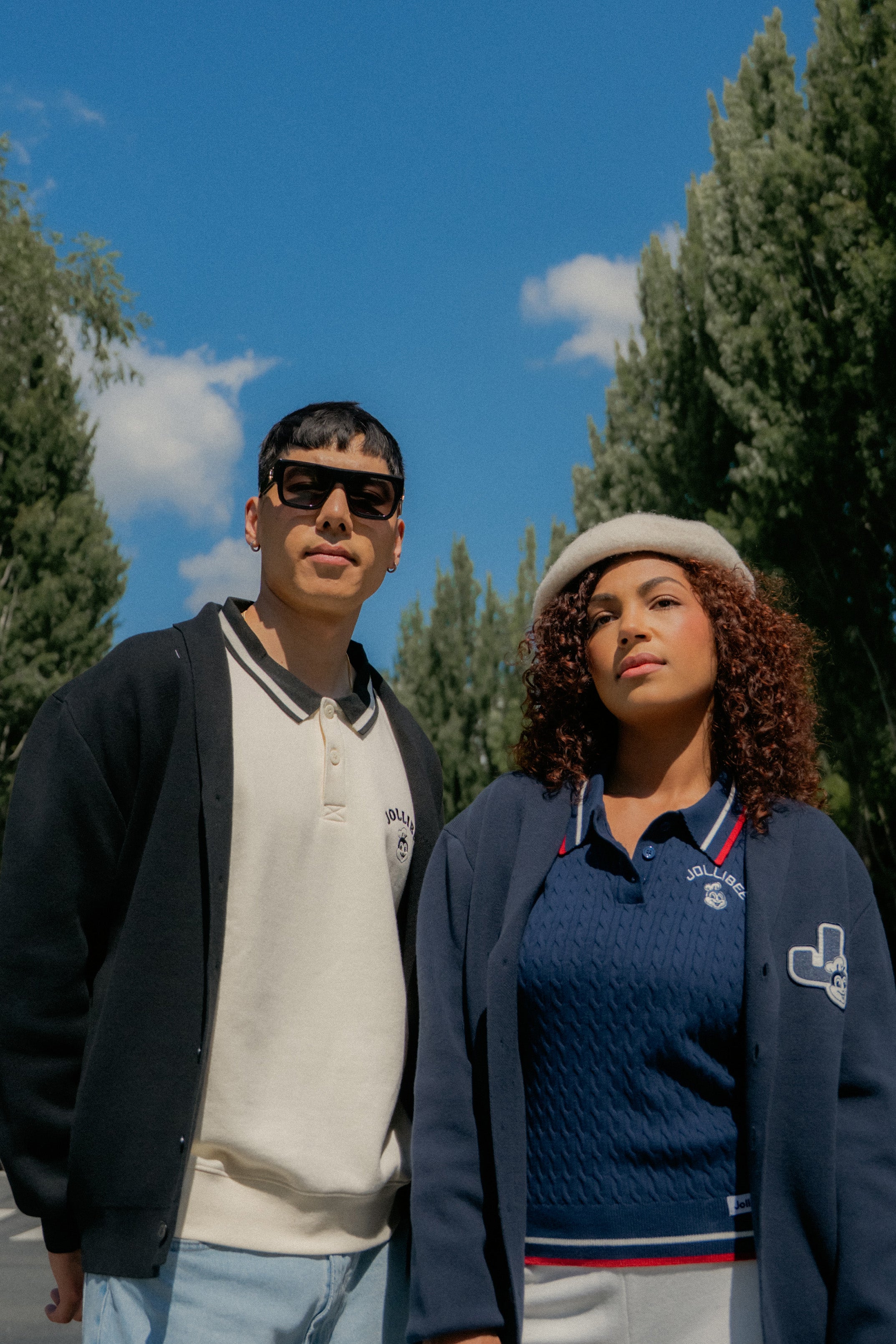Two people standing outdoors with trees and blue sky in the background