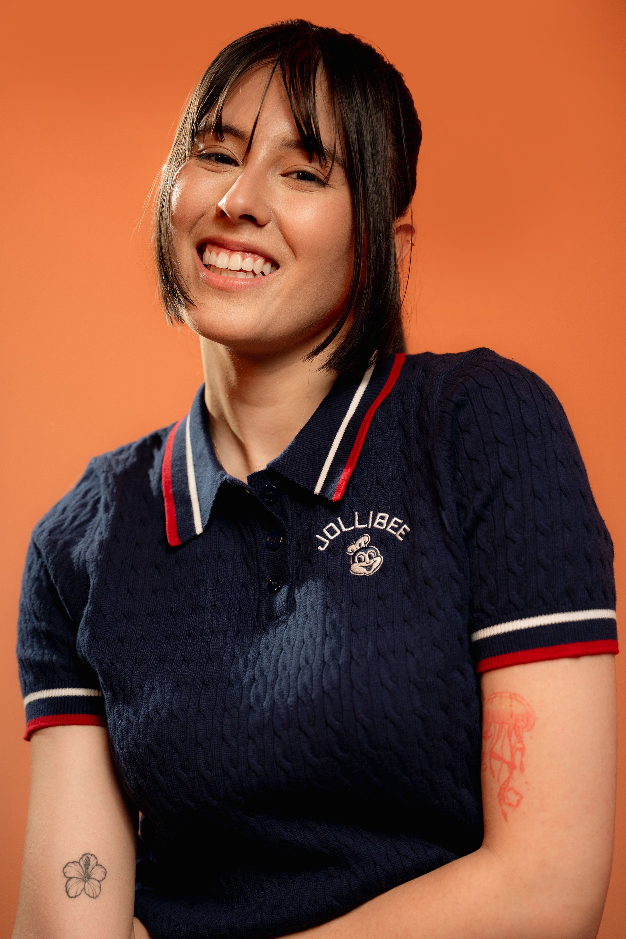 Person wearing a navy blue polo shirt with Jollibee logo on an orange background