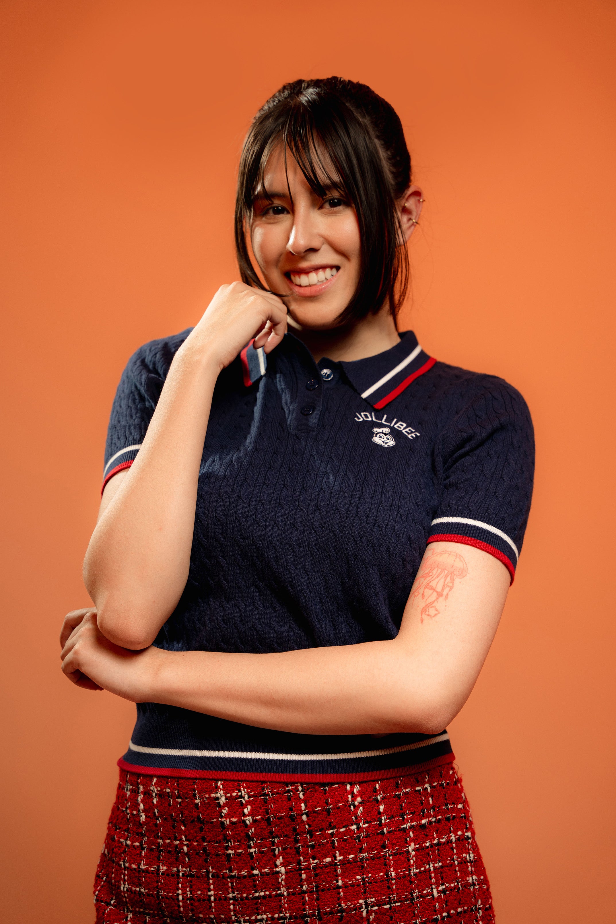 Woman wearing a navy blue polo shirt with red and white trim against an orange background