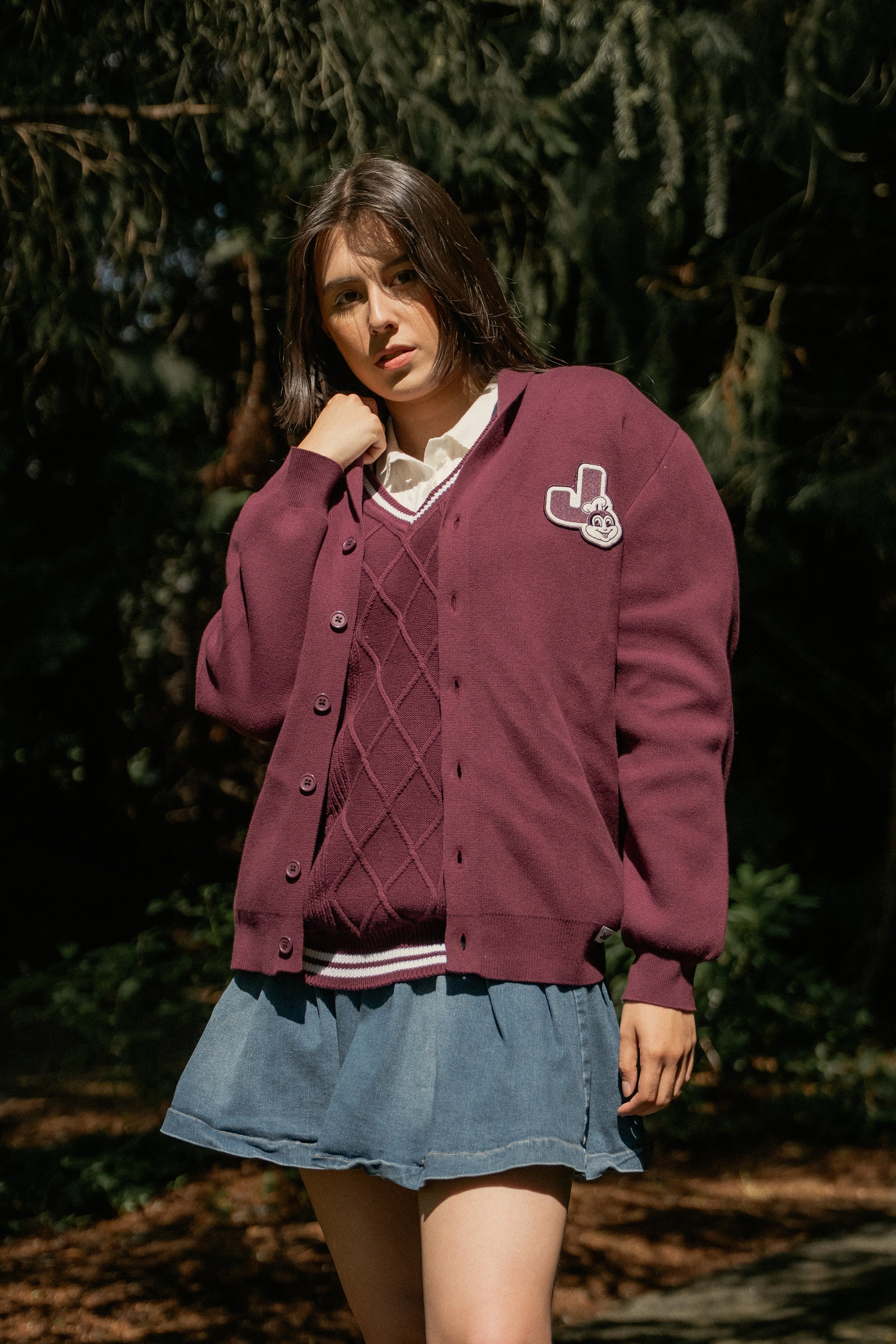 Woman wearing a maroon cardigan with a Jollibee logo in a forest setting