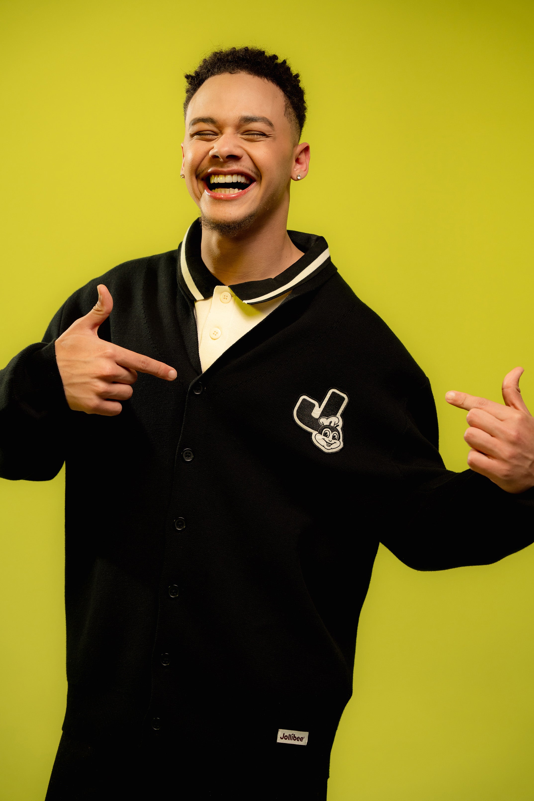 Person wearing a black cardigan with a logo on a yellow background
