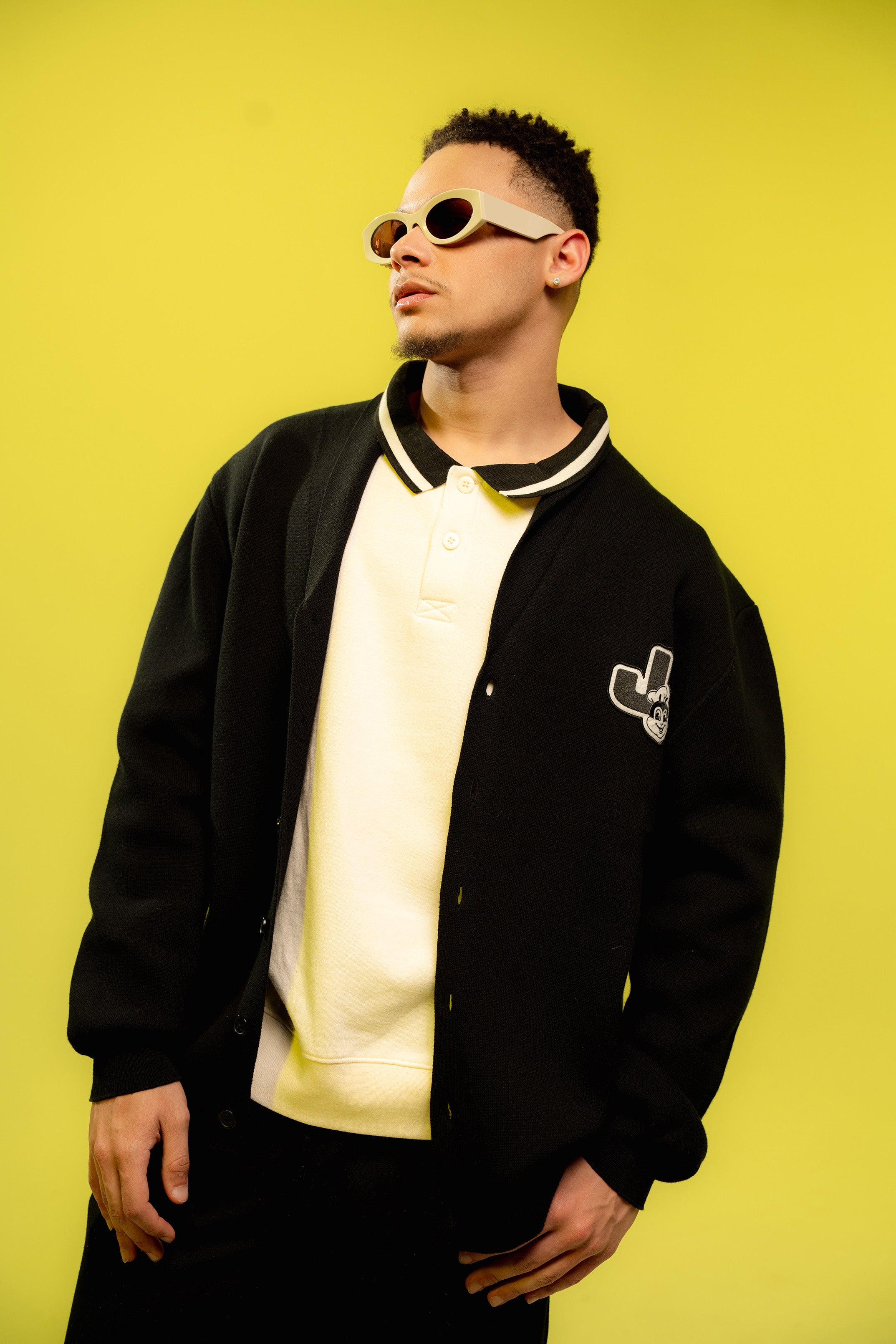 Person wearing a black cardigan with a logo on a yellow background