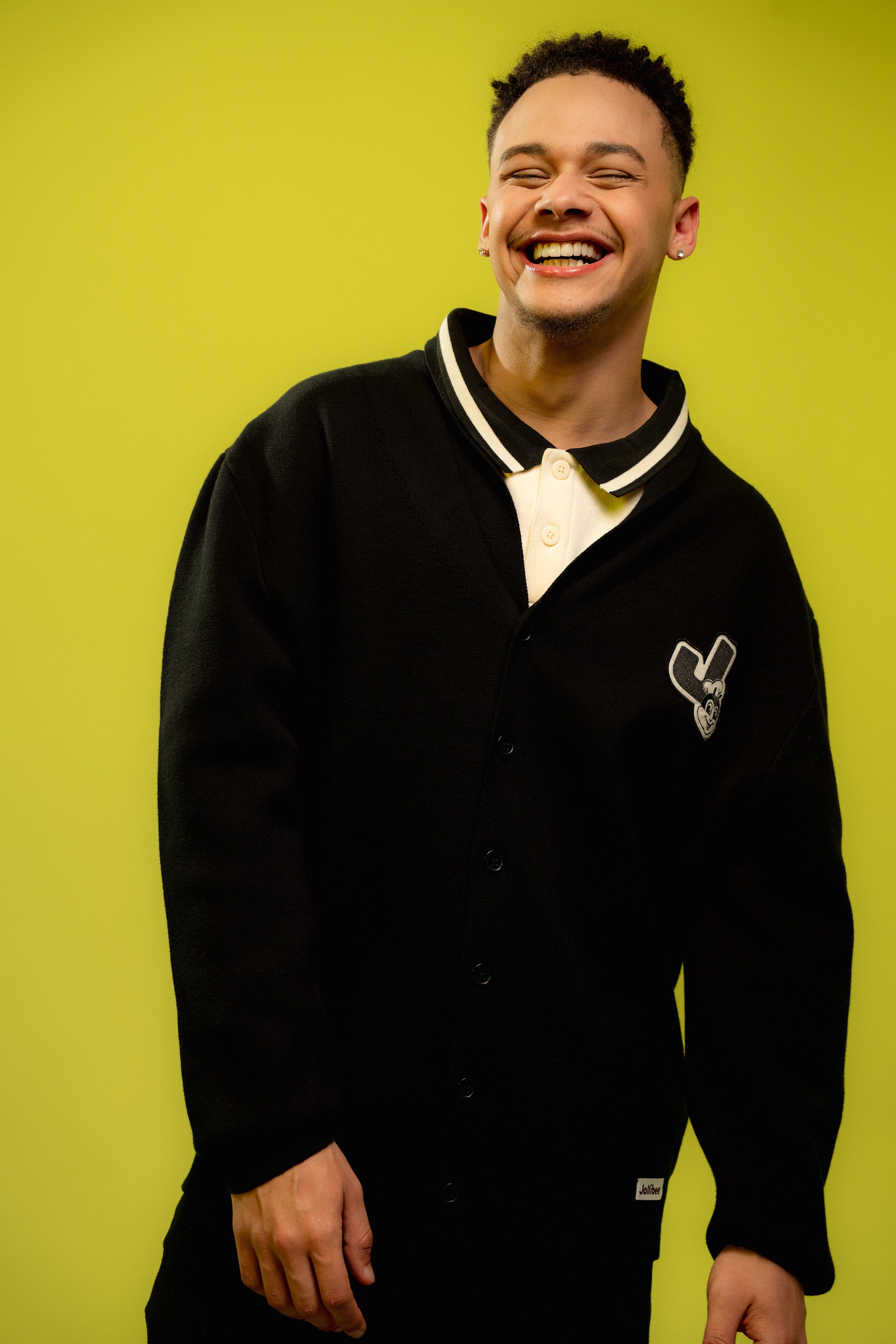 Person wearing a black varsity cardigan with a logo on a green background