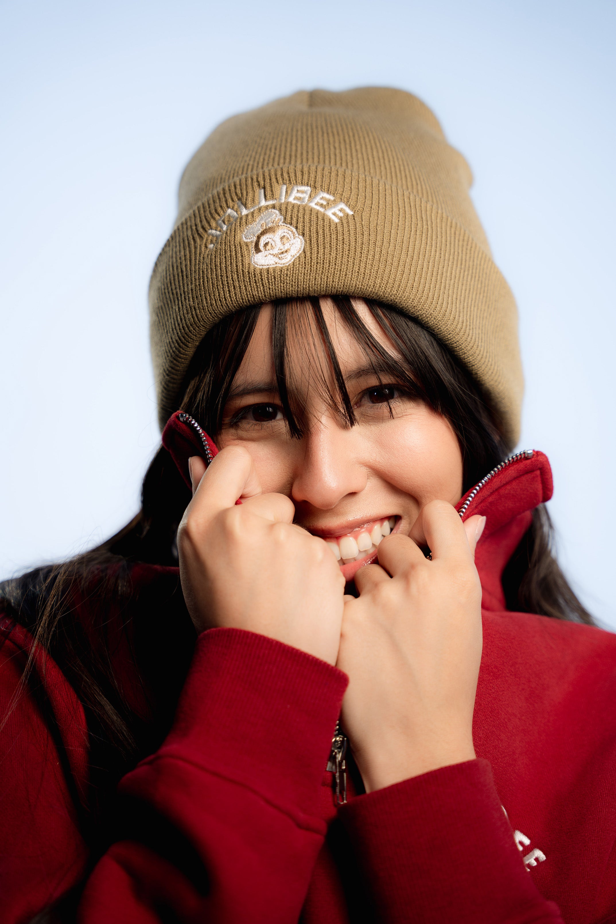 Person wearing a beige beanie and red jacket with a light blue background