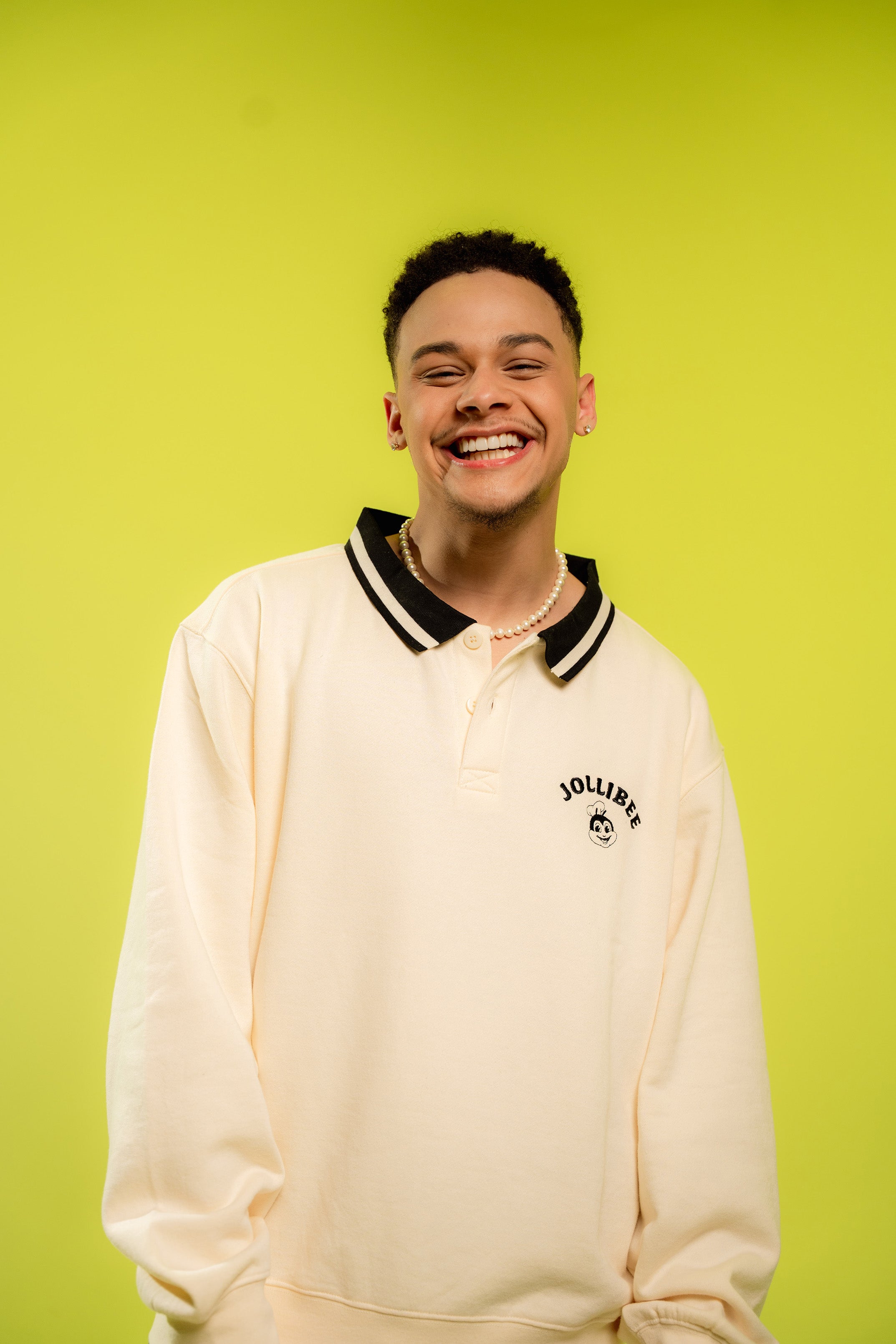 Person wearing a cream-colored sweater with black trim against a bright green background