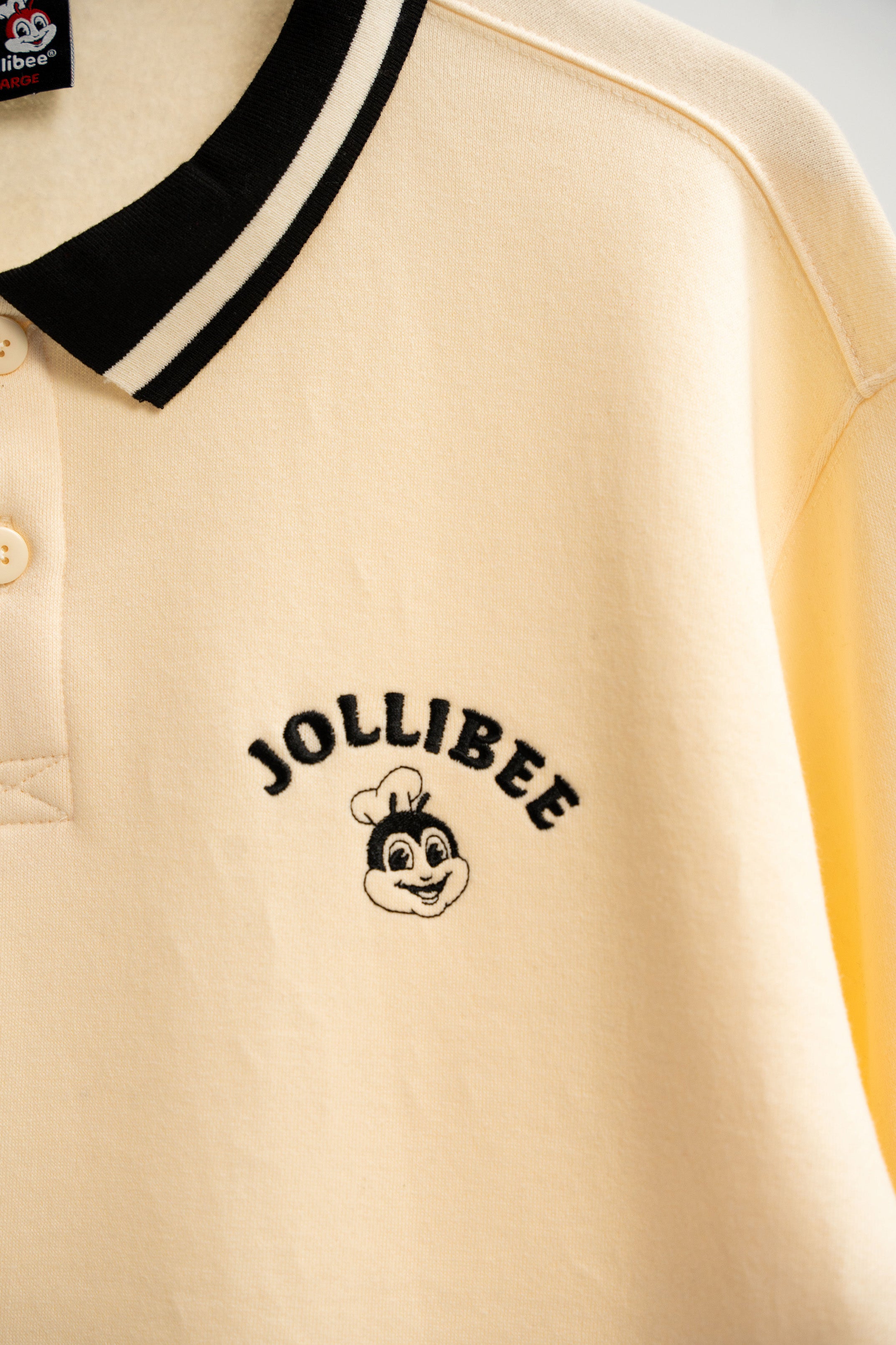 Beige shirt with black collar and Jollibee logo on a beige background