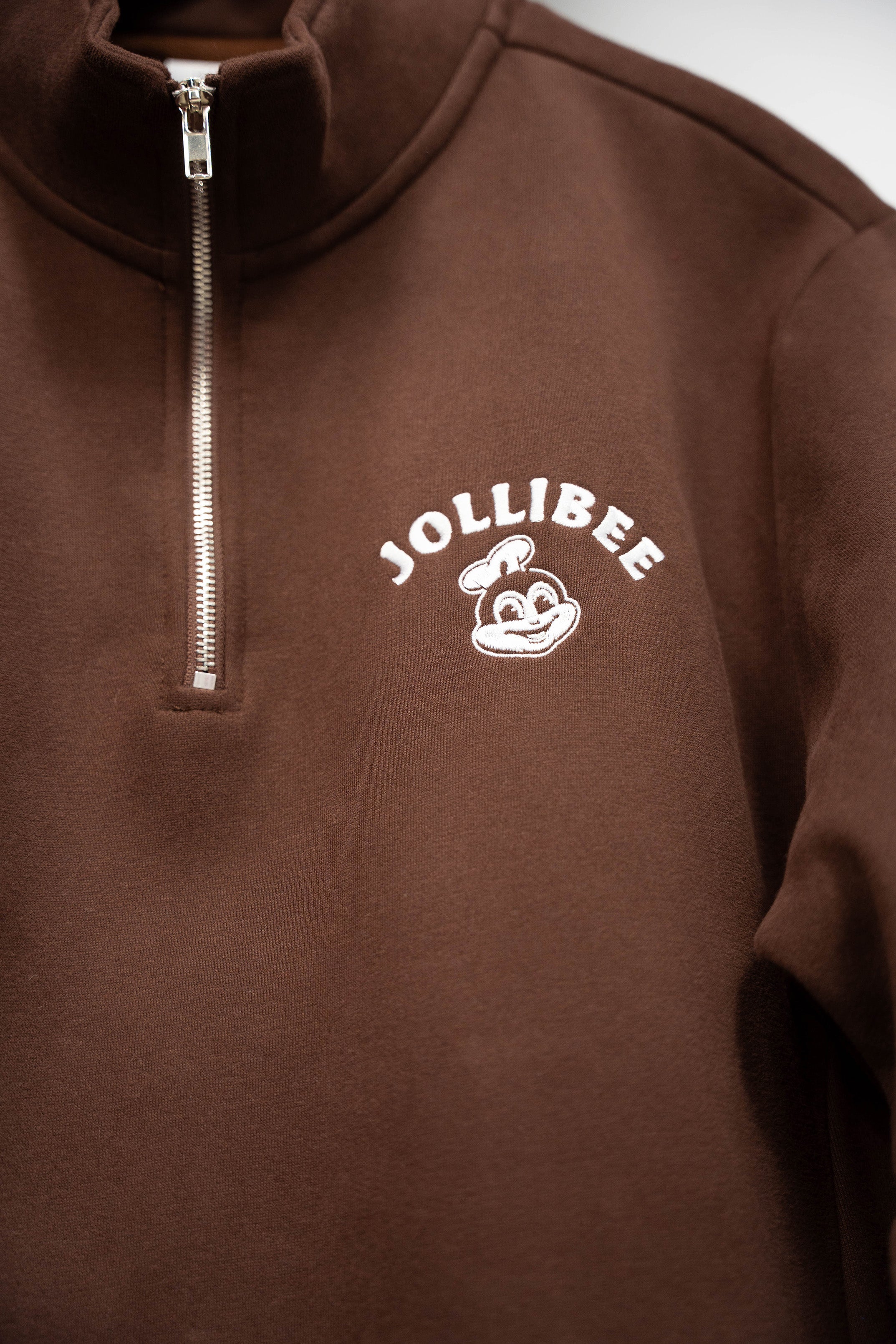 Brown quarter-zip sweatshirt with Jollibee logo on a plain background