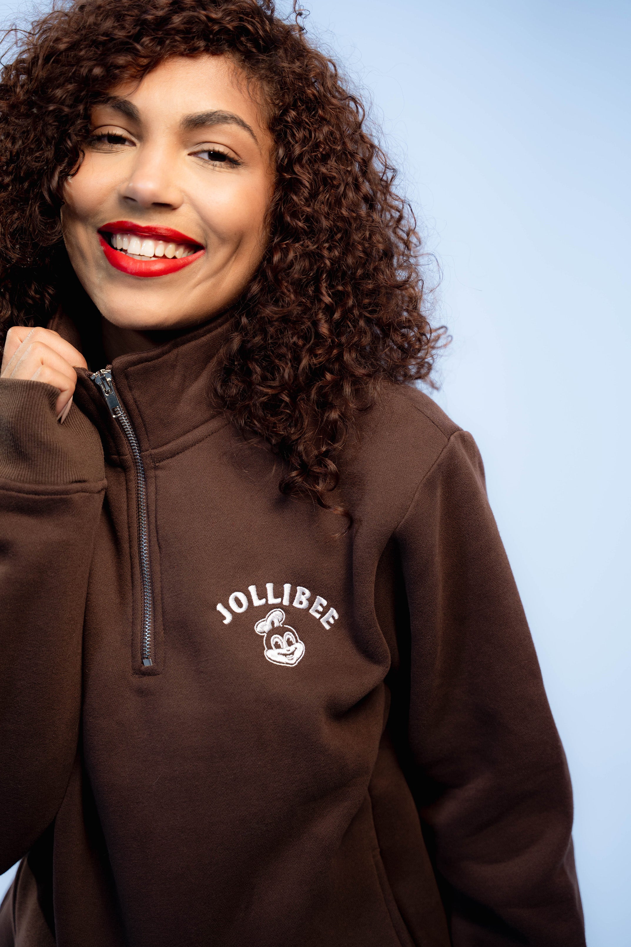Person wearing a brown jacket with Jollibee logo against a light blue background