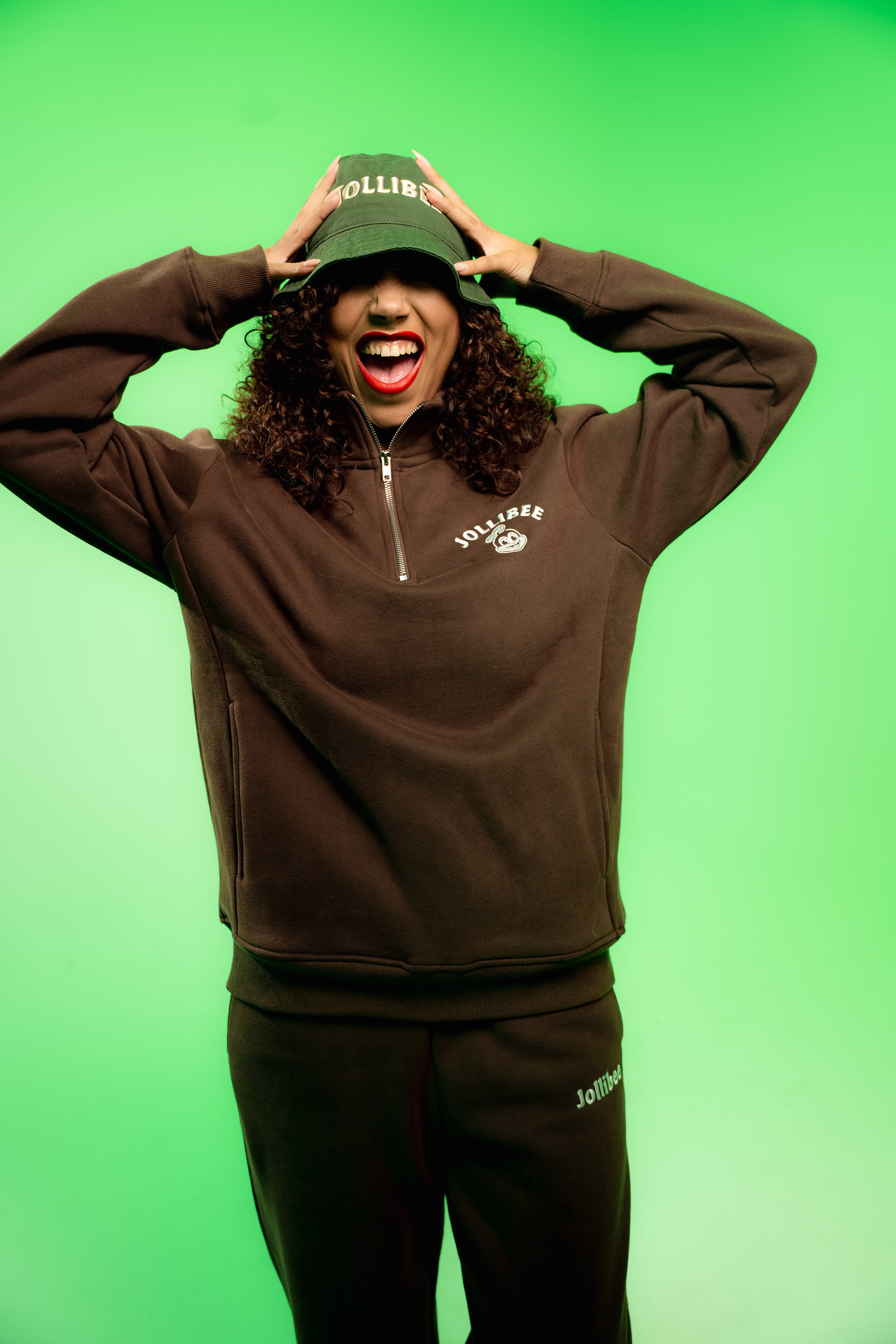 Person wearing a brown tracksuit with a green cap on a green background