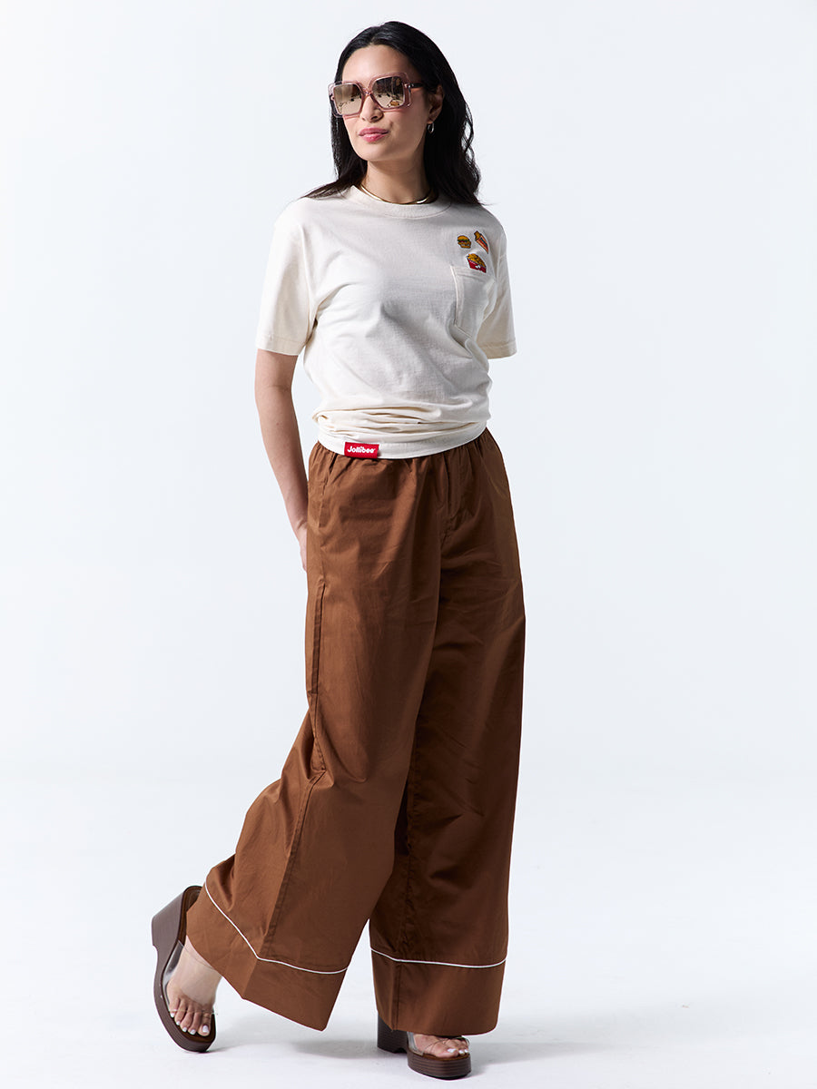 A young woman wearing sunglasses and a beige t-shirt with a pocket and three illustration graphics of Jollibee products on the side on a white background.
