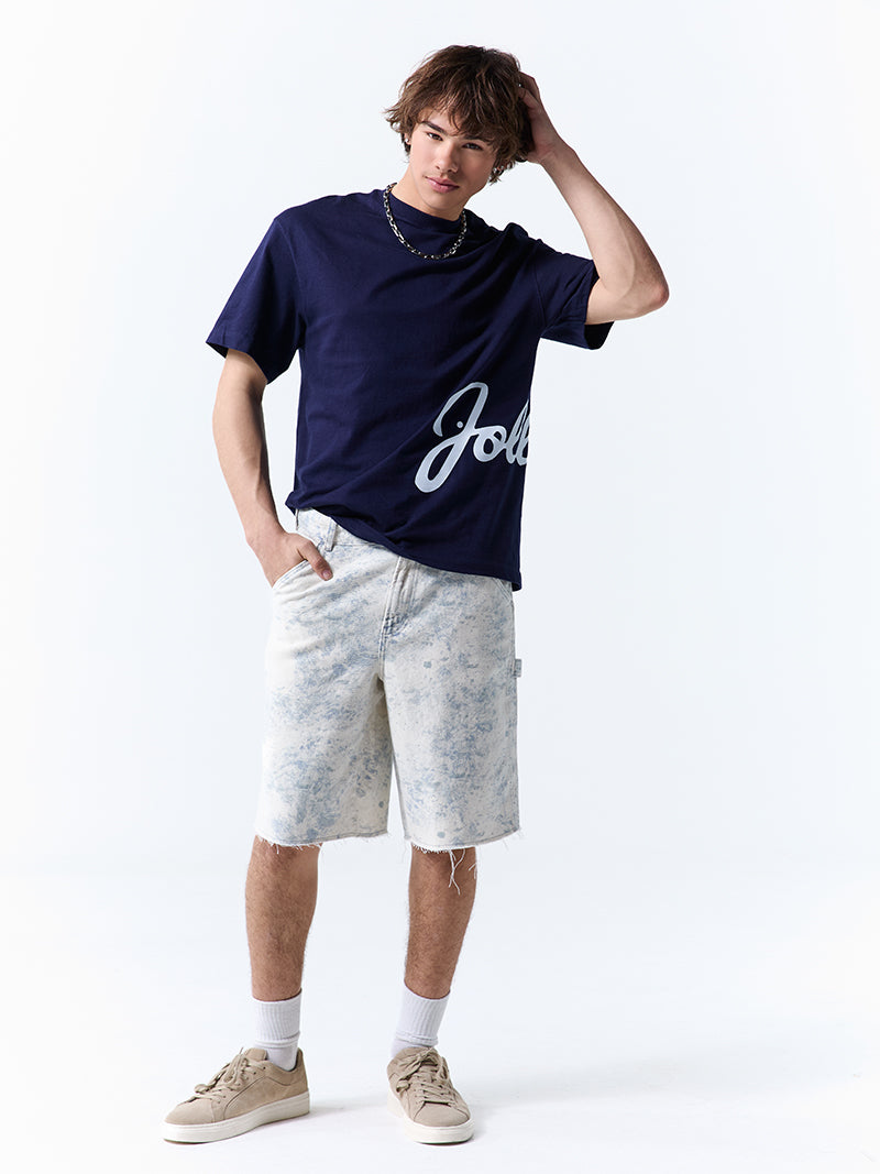A young man wearing a navy t-shirt with 'Jollibee' in script on the side on a white background.